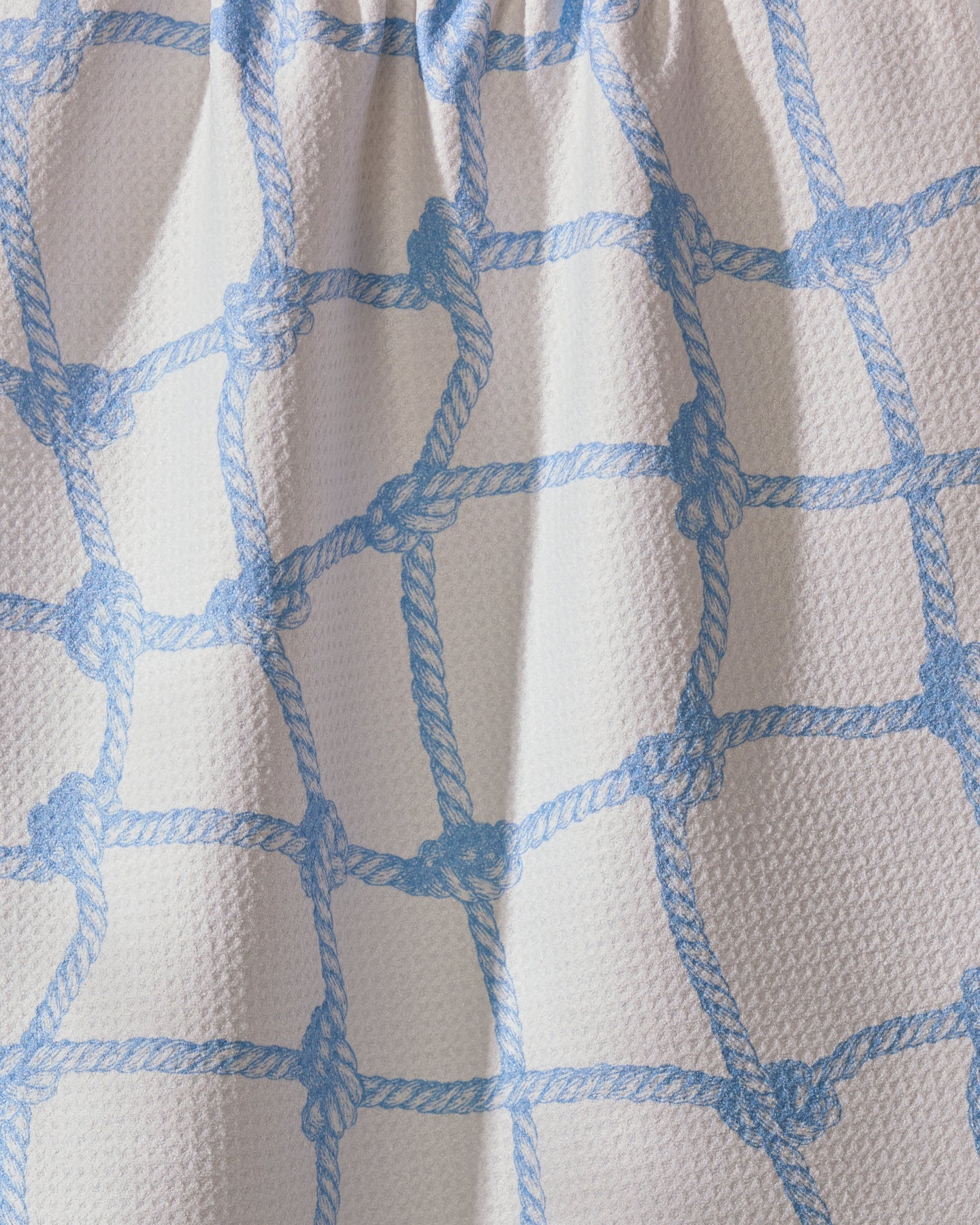 A close-up of Geometry’s Tethered Blue dish towel shows ultra-absorbent white fabric with a light blue rope net pattern, soft folds, and shadows that highlight both its practical design and stylish texture.