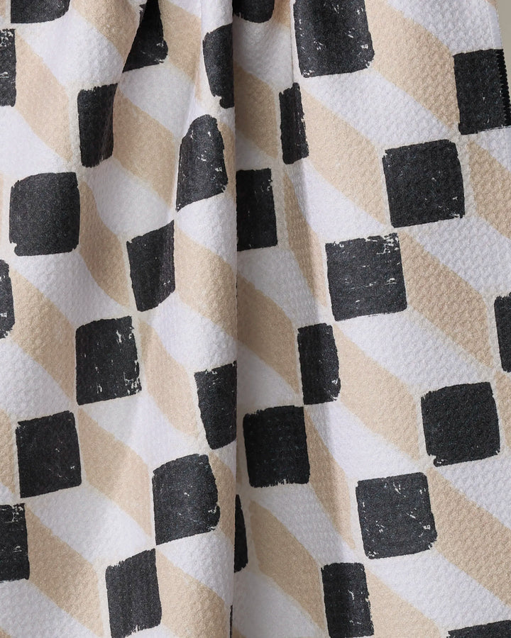 A close-up of Tessera by Studio Jeannot shows textured fabric with alternating black squares and beige diamonds on white, perfect as a stylish kitchen towel made from recycled materials.