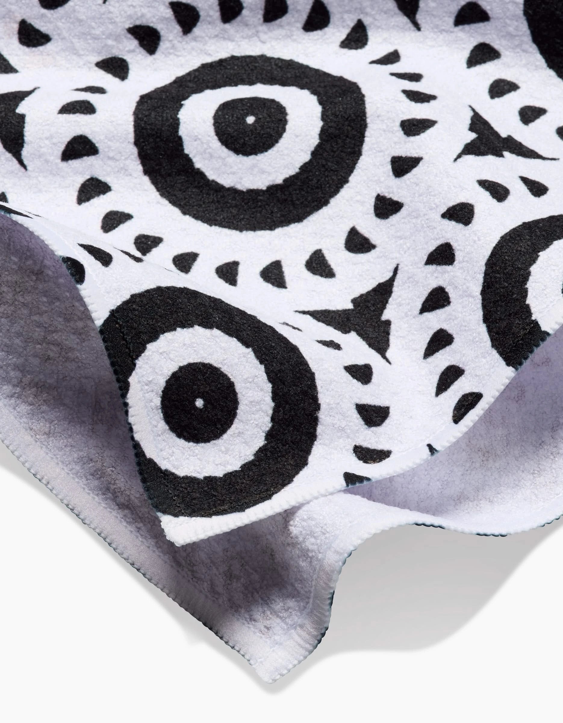 A close-up of the Texas Two Step tea towel by Katherine Berkeley, crafted from recycled materials with black concentric circles and angular patterns. The edge of the Geoweave fabric is slightly curled.
