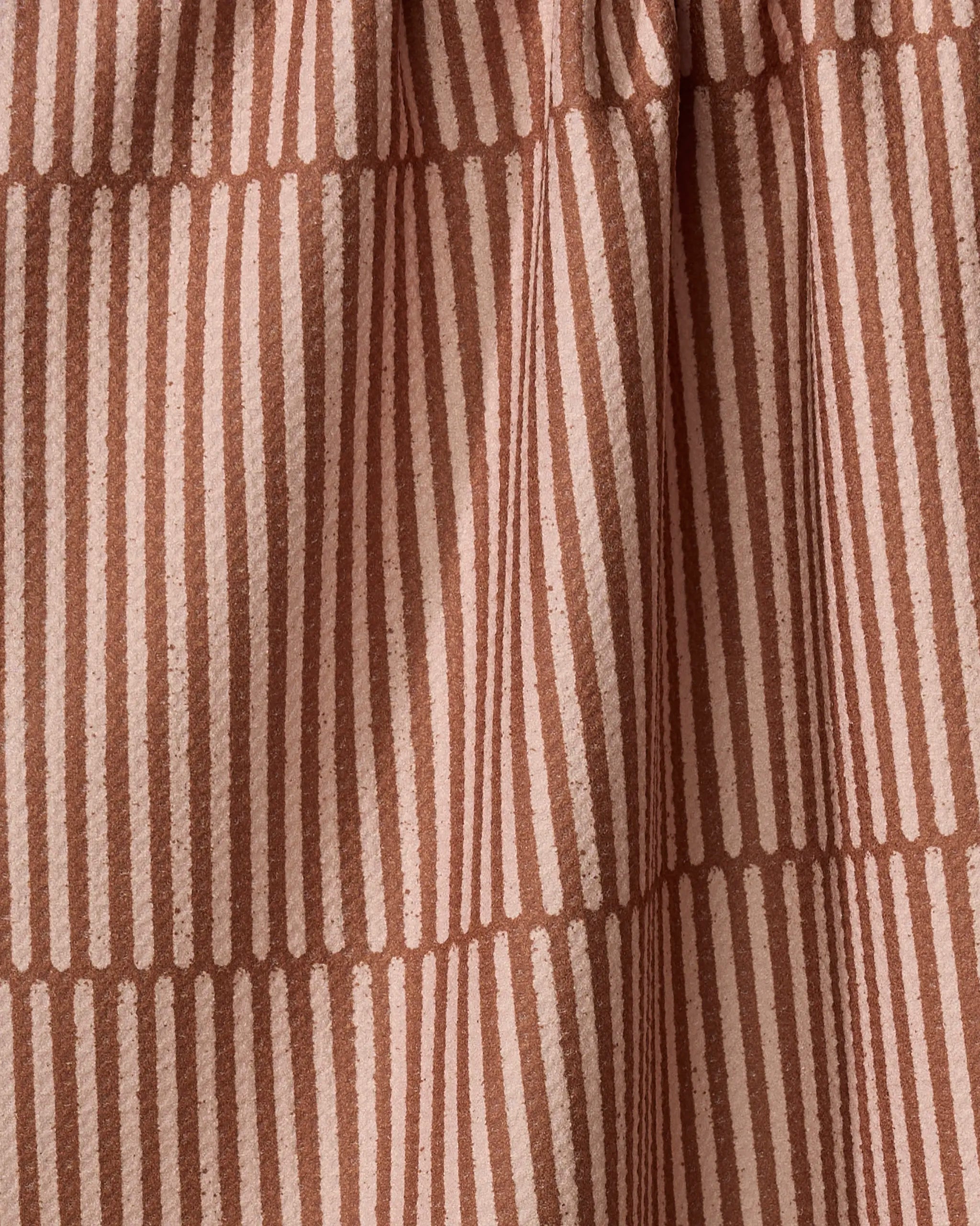 A close-up of Rosa Kichline's Textured Stripe recycled kitchen towel, featuring vertical and horizontal light pinkish-beige stripes on a dusty rose background in a geometric grid pattern with soft folds and texture.
