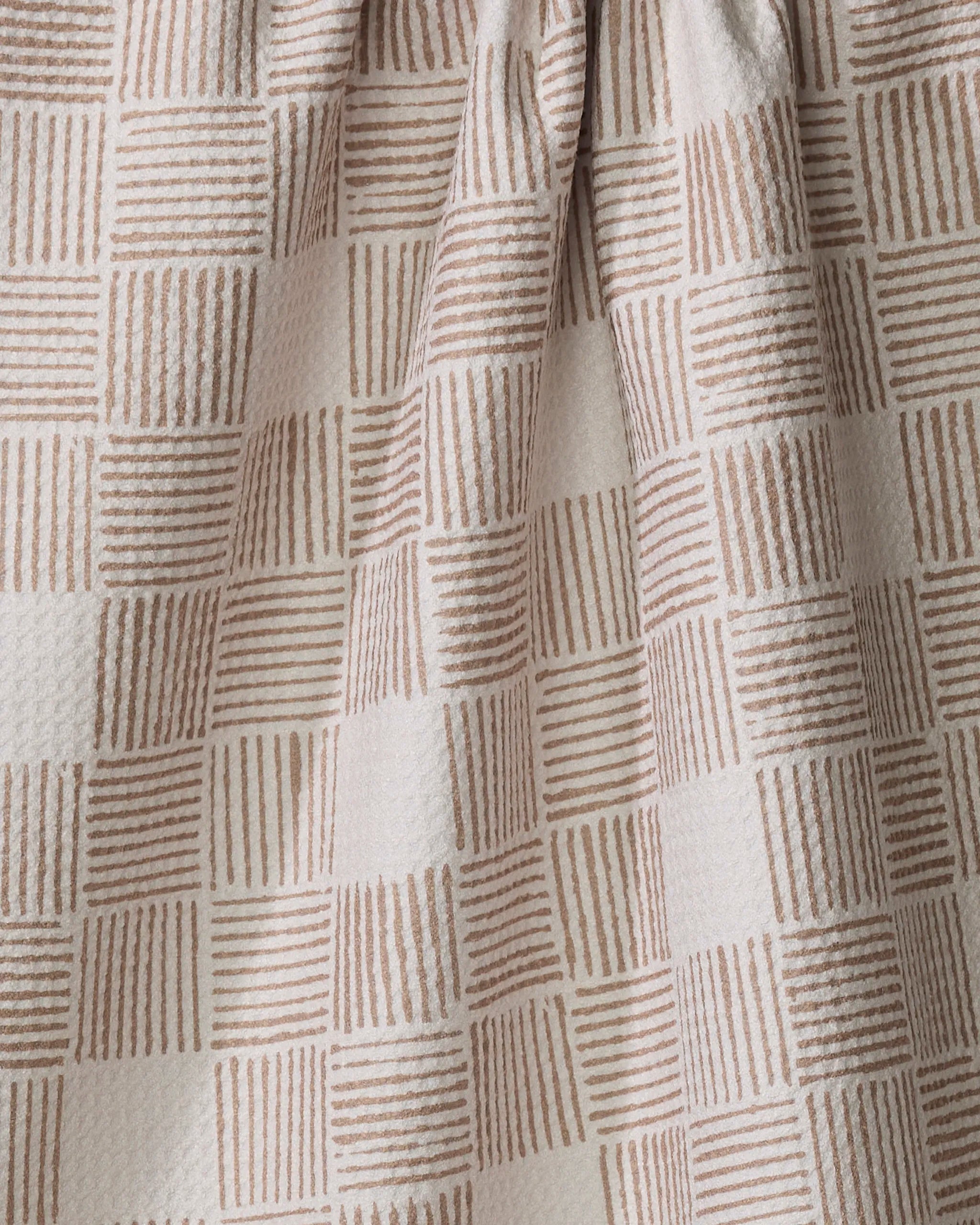 Close-up of the Thatcher kitchen towel by Studio Jeannot, showing a beige and light cream grid pattern with alternating squares of horizontal and vertical lines. The fabric is slightly gathered at the top.