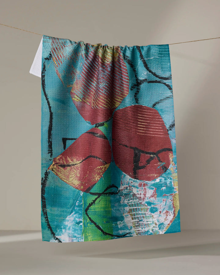 Katherine Berkeley’s “The Apple Doesn’t Fall Far From the Tree” tea towel features a colorful abstract design with red shapes, black lines, and a blue-teal background, made from recycled materials and perfect for brightening your kitchen.