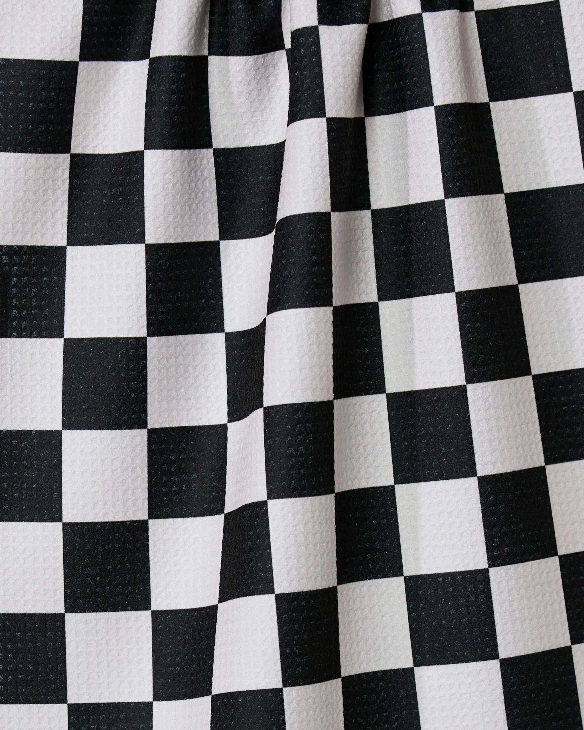 A close-up of GEOMETRYs The Classic shows a black and white checkered kitchen tea towel with a subtle textured surface and gentle folds, creating slight distortions in the straight lines of the squares.