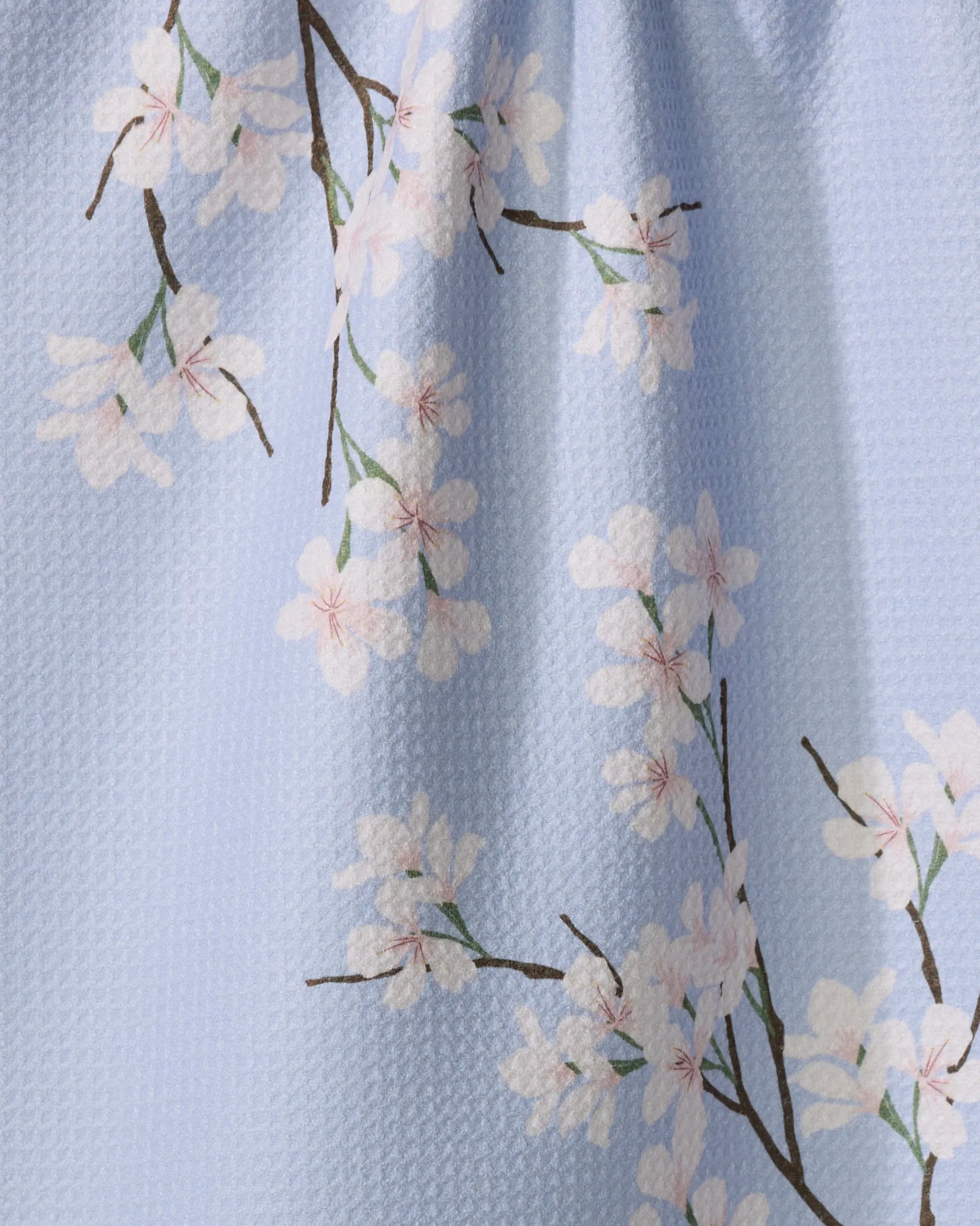 The Eve by Becki Owens is a light blue Geoweave tea towel adorned with white cherry blossom branches and pink centers, made from recycled materials.