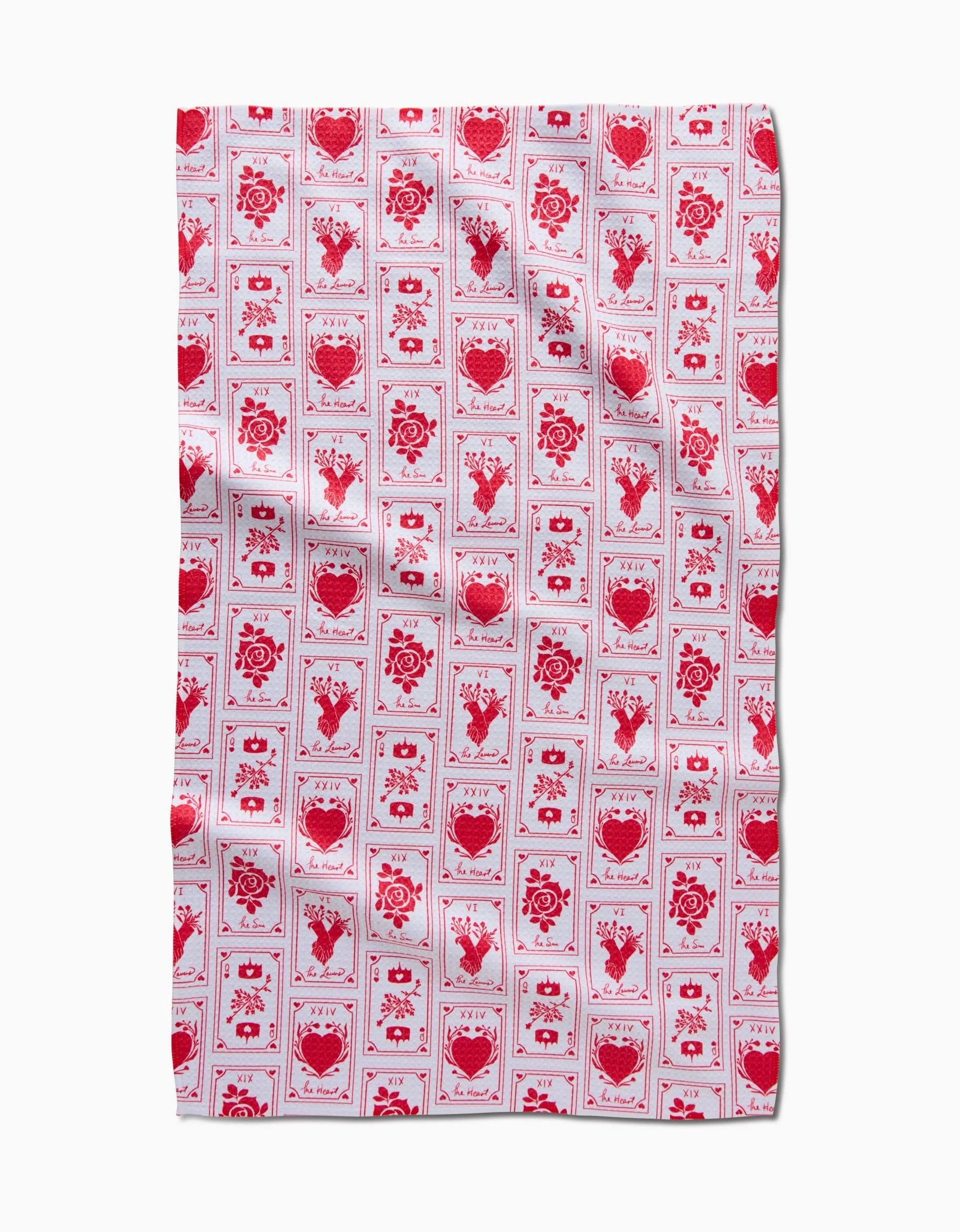 The Lovers Tea Towel by Danelys Sidron features a red and white grid of hearts, roses, and floral motifs on a white background. Made from recycled materials, the fabric has a subtly wrinkled texture.