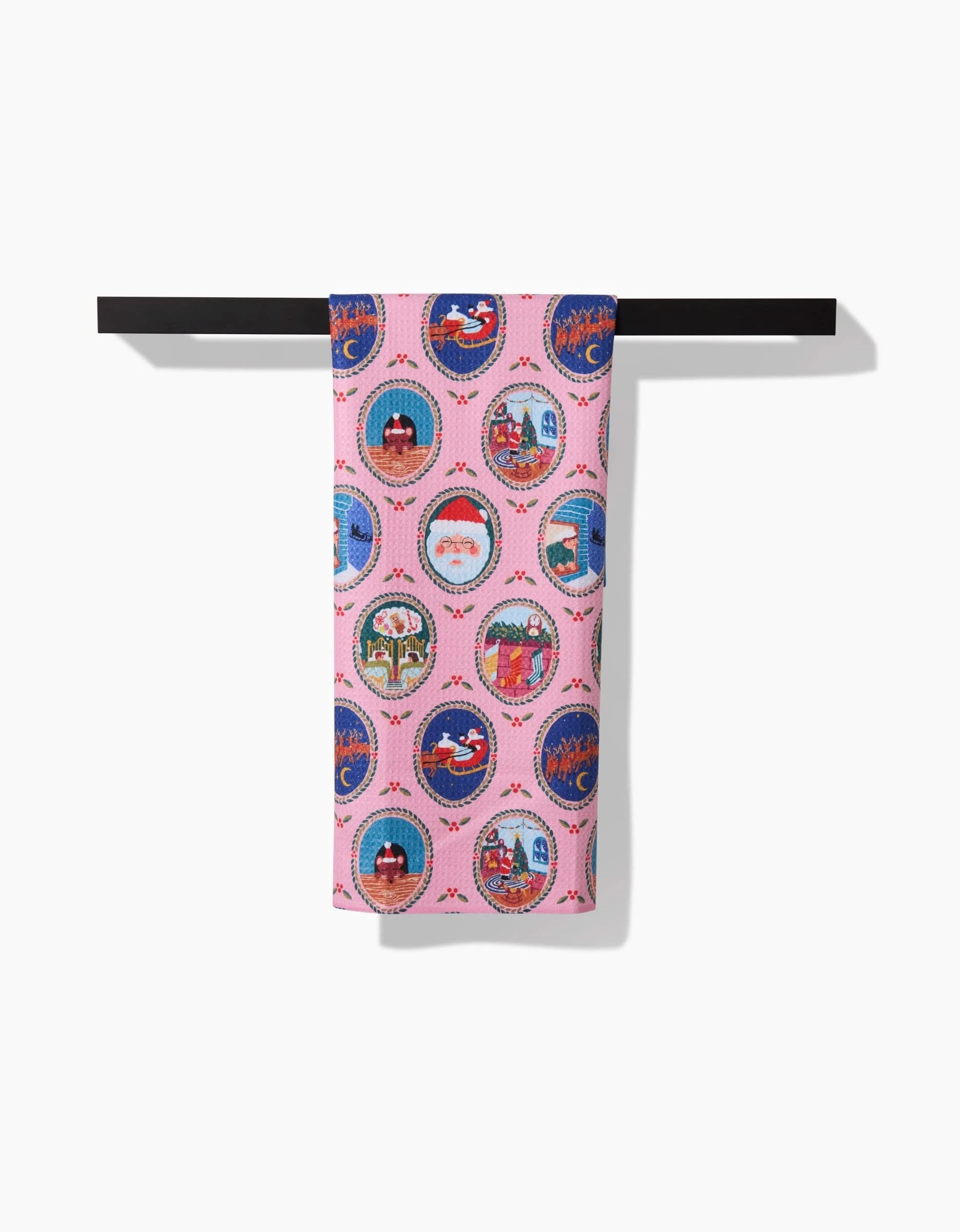 The Night Before Christmas quick-drying towel by Elisabeth Wing features pink fabric with circular holiday designs like Santa, reindeer, and snowy houses, neatly draped over a black bar against a white background.