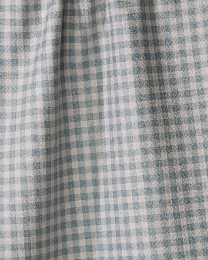 A close-up of the Jenny Keller Tidepool Check kitchen towel showcases its blue and white grid of small squares. Made from recycled materials, the fabric appears slightly gathered or pleated near the top.