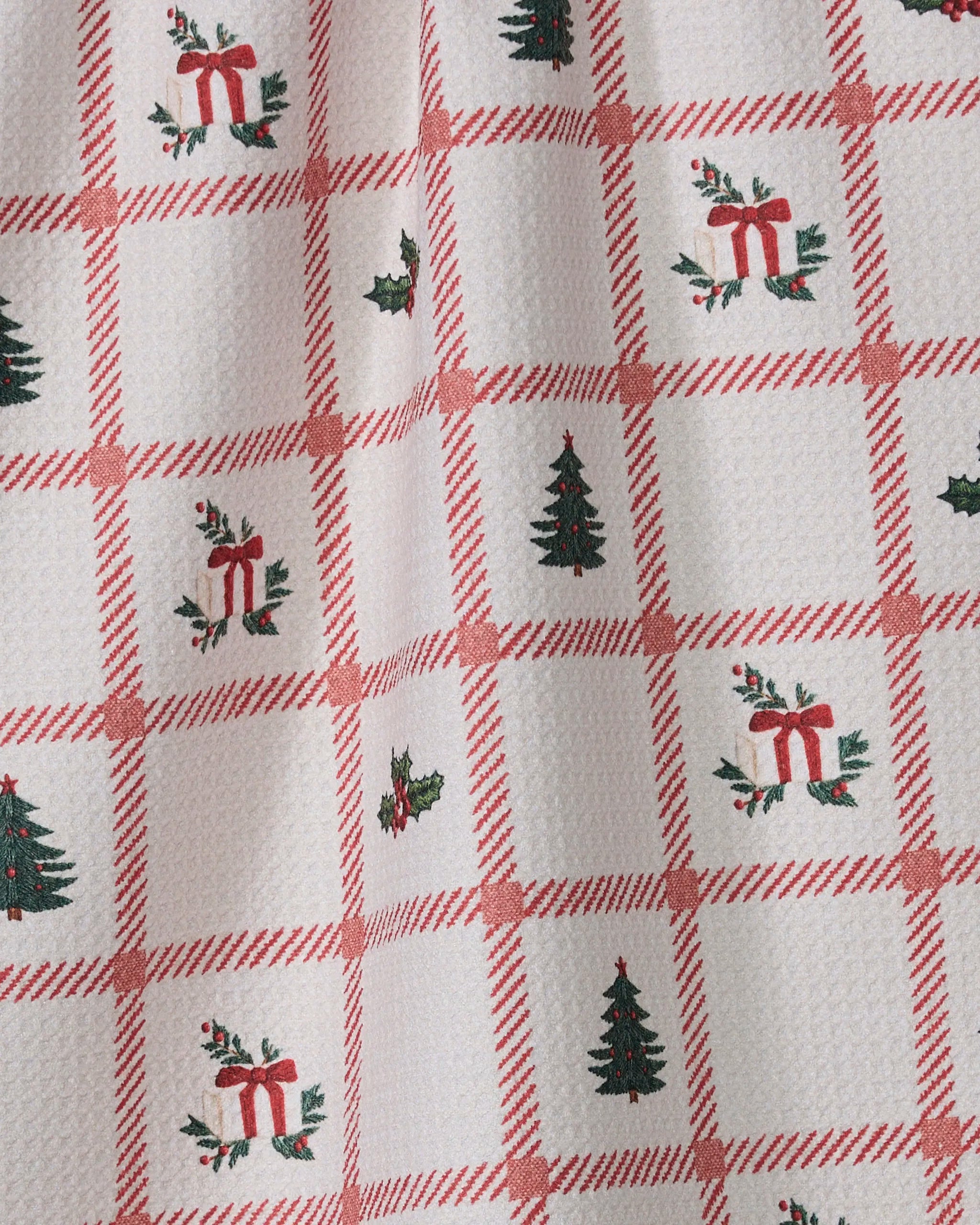 The Geometry Tidings tea towel features a white textured fabric with a red plaid pattern, showcasing festive green trees, red gift boxes, and holly in alternating squares—perfect for quick-drying in your holiday kitchen.