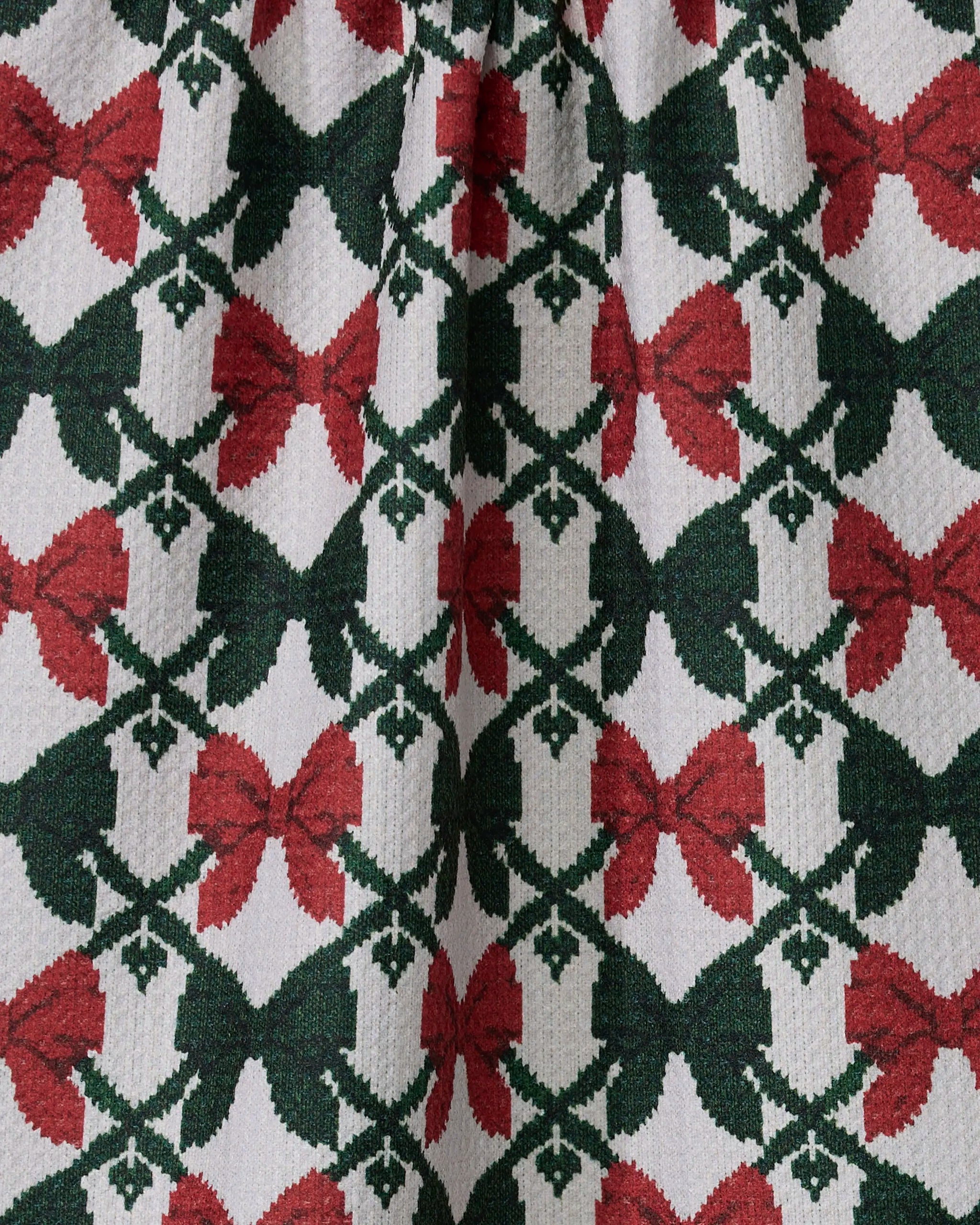 Close-up of Geometry’s "Tied" recycled kitchen towel, showcasing rows of red and dark green bows connected by green lattice lines on a textured white background.
