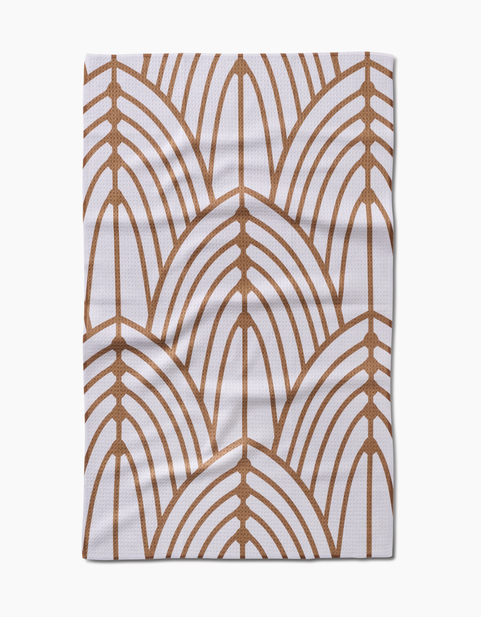 The Tiffany cloth by Amy MacCready is made of white Geoweave fabric and showcases a repeating brown geometric pattern of overlapping arch shapes, similar to stylized leaves or fans, with visible folds and creases.