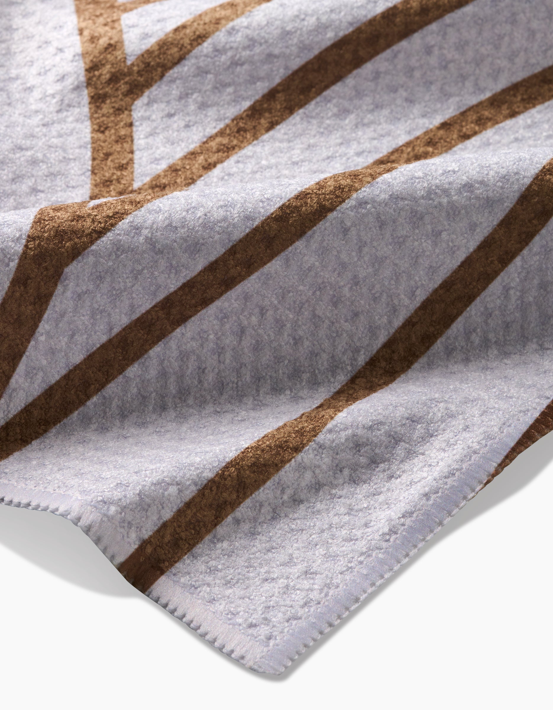 A close-up of the Tiffany blanket by Amy MacCready, made from Geoweave fabric in soft gray with brown geometric lines and detailed edge stitching.