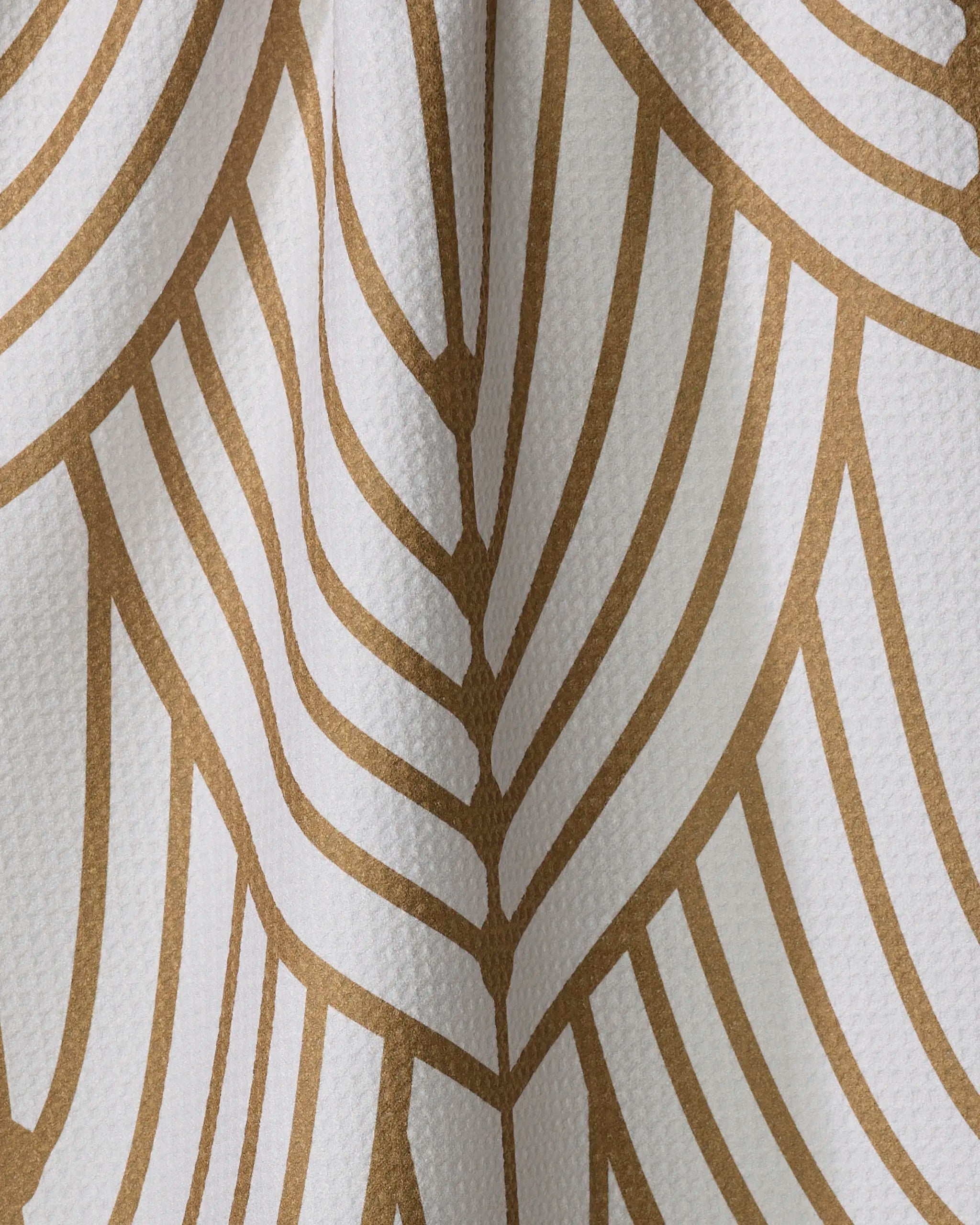 Close-up of the Amy MacCready "Tiffany" white kitchen towel, showcasing a geometric gold leaf or feather pattern. Made from recycled materials for an eco-friendly touch.