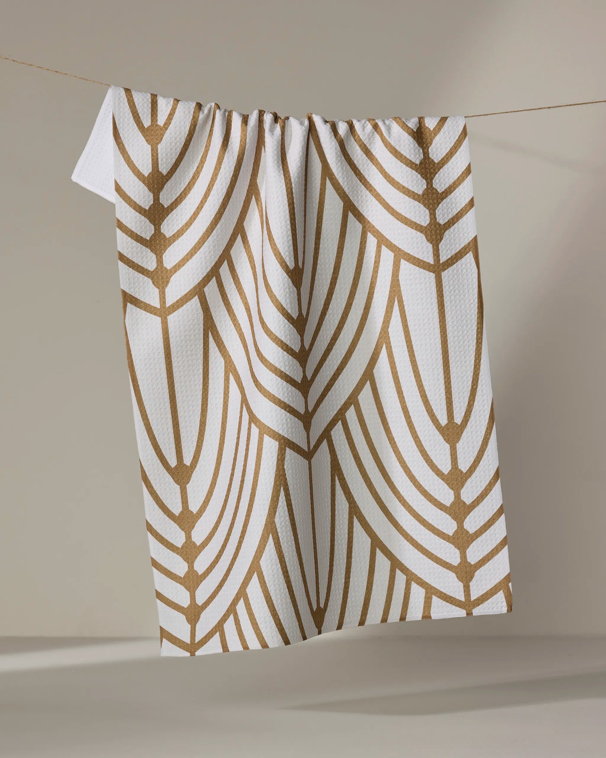 The Tiffany kitchen towel by Amy MacCready features a bold brown geometric leaf pattern on white and hangs stylishly against a neutral background, making it an ideal accent for your space.