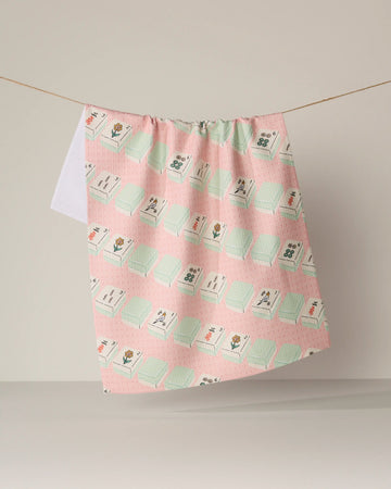 The Geometry "Tile Parade" kitchen tea towel, featuring a pink and green floral and tile pattern and crafted from durable Geoweave fabric, hangs on a string against a neutral background.