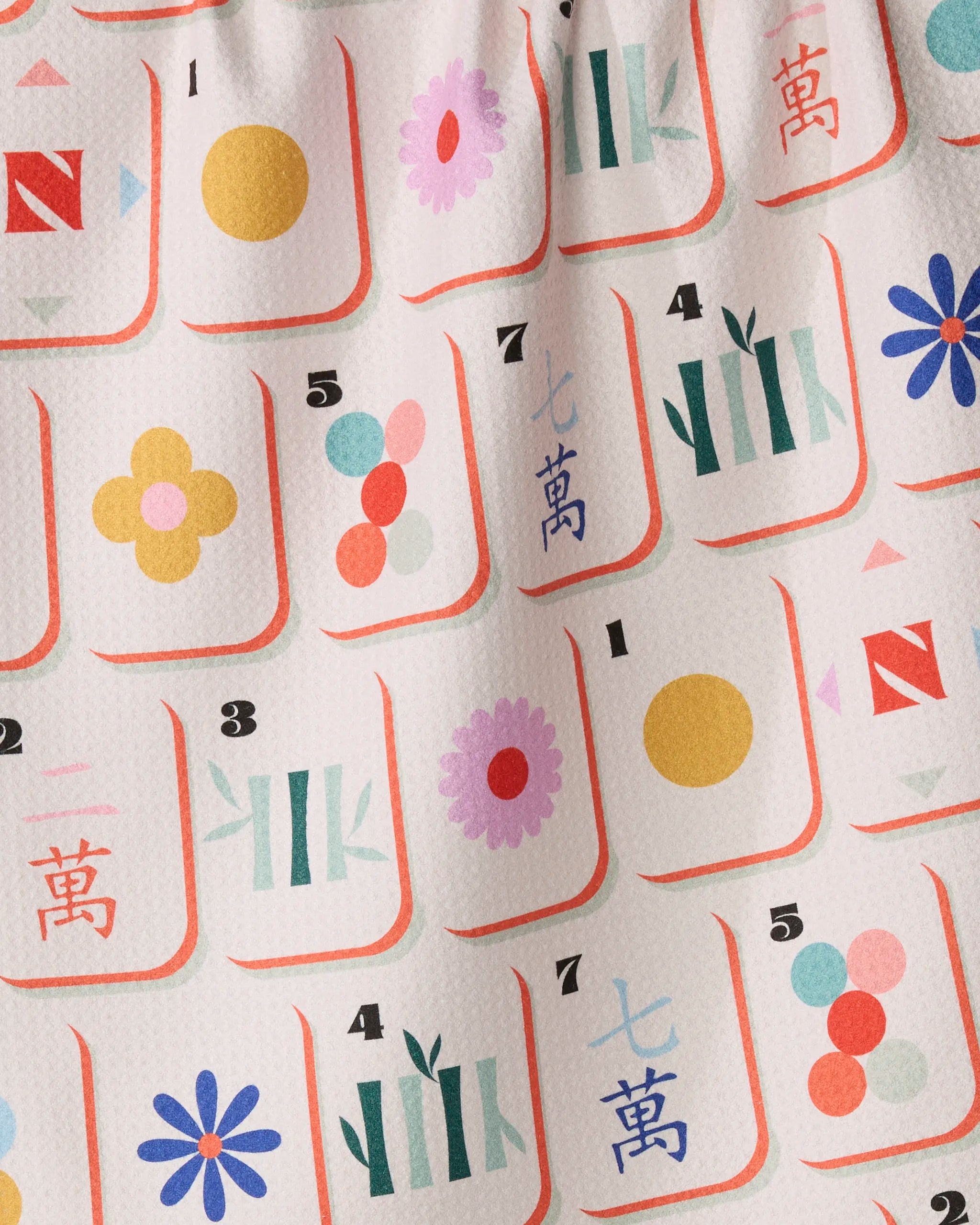 Tile Toss by Geometry is a patterned fabric tea towel showcasing stylized Mahjong tiles—including numbers, flowers, circles, bamboo, and Chinese characters—in vibrant colors on a white background. This quick-drying towel adds a playful touch to your kitchen essentials.