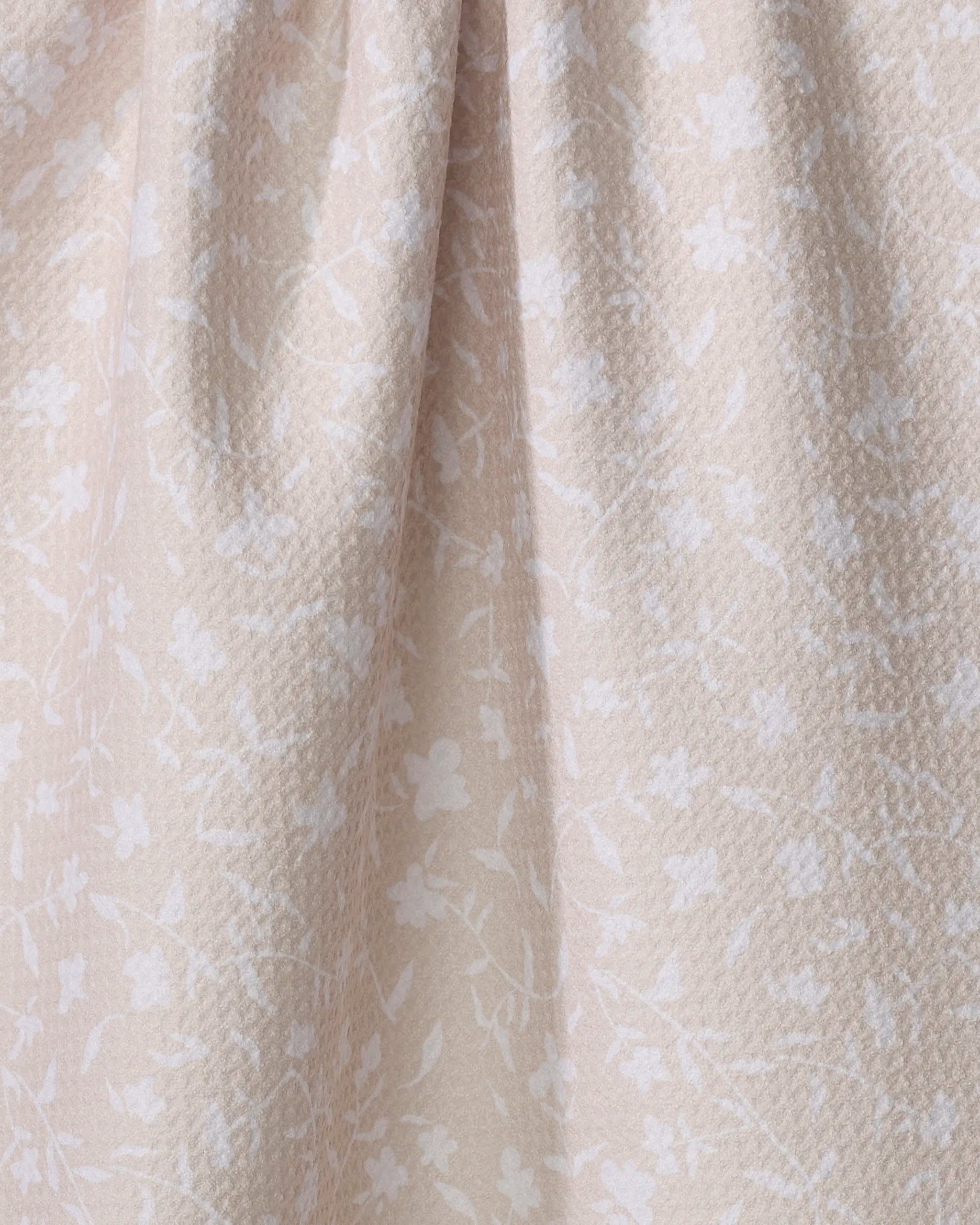 Close-up of the Aubrey Fairchild Tiny Floral tea towel in beige, featuring a subtle white floral pattern and gentle folds. Made from ultra-absorbent recycled materials for style and sustainability.