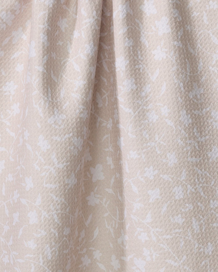 Close-up of the Aubrey Fairchild Tiny Floral tea towel in beige, featuring a subtle white floral pattern and gentle folds. Made from ultra-absorbent recycled materials for style and sustainability.