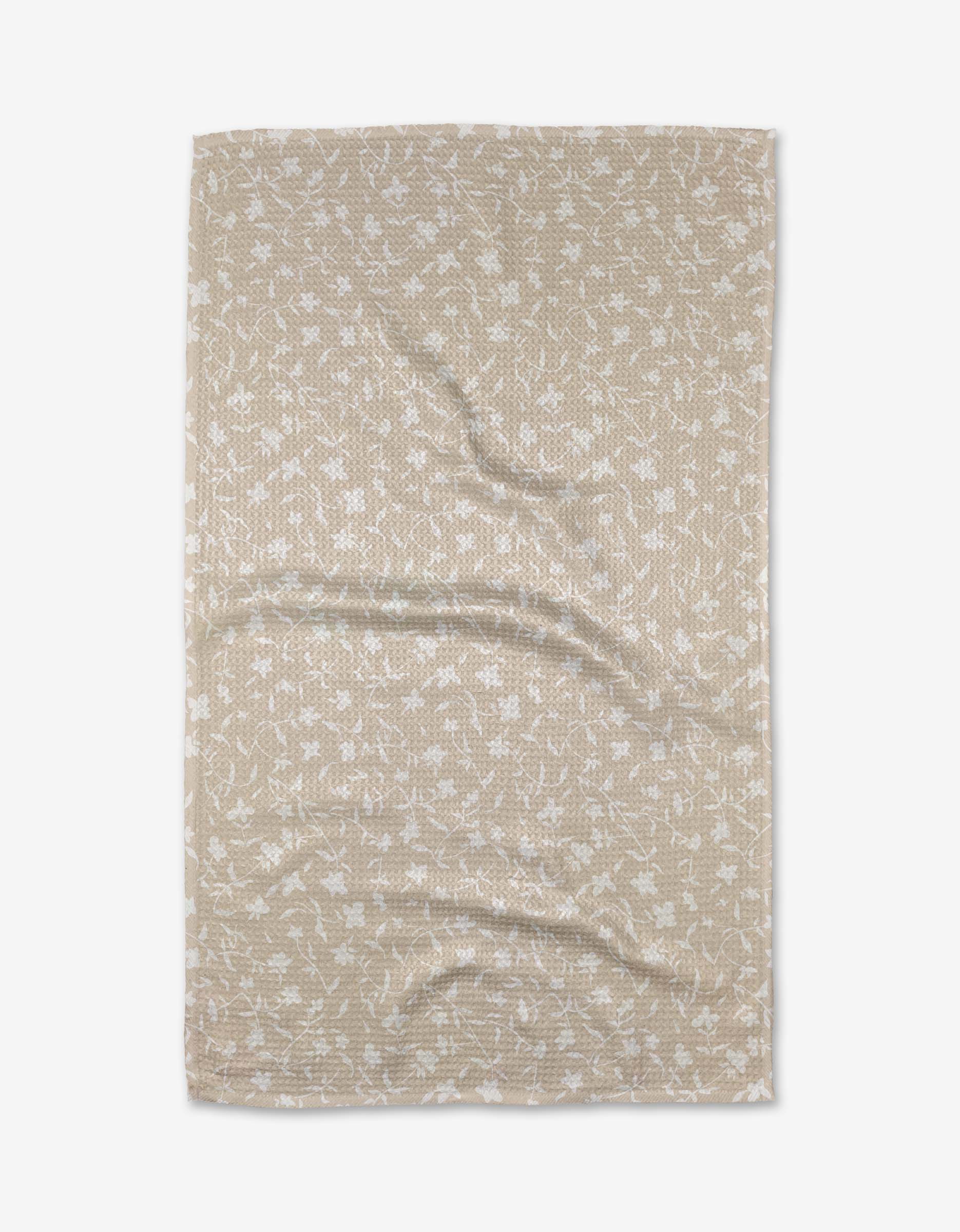 The Tiny Floral bath towel by Aubrey Fairchild is beige and rectangular, made from Geoweave fabric with a subtle white floral pattern, shown flat with gentle creases.