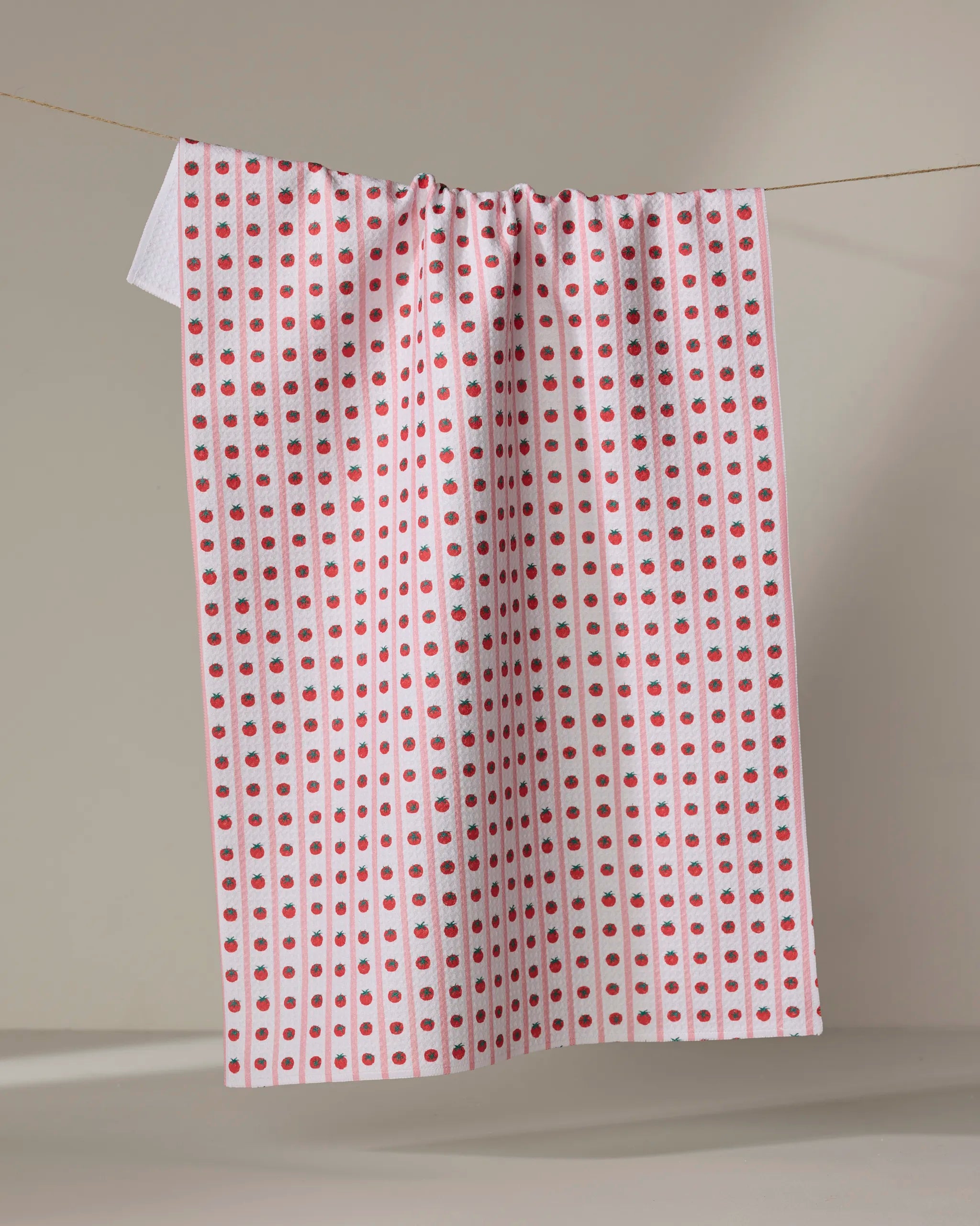 The Tomato Stripes tea towel by Brittany Jepsen features vertical rows of small red dots with occasional blue-green accents, hanging against a plain, neutral background.