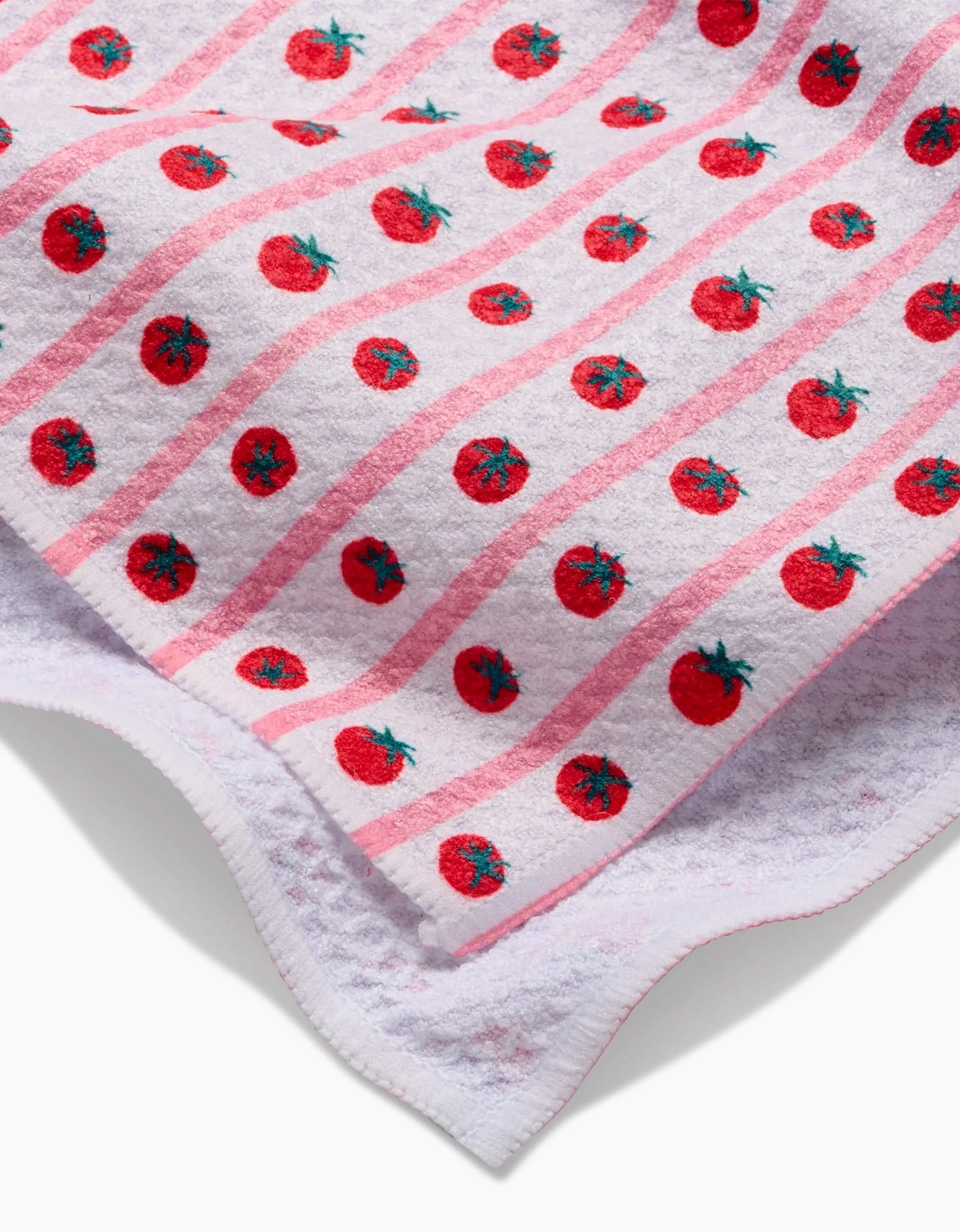 The Brittany Jepsen Tomato Stripes tea towel features pink stripes and red tomato motifs on white Geoweave™ fabric, made from post-consumer recycled materials, shown partially folded on a white background.
