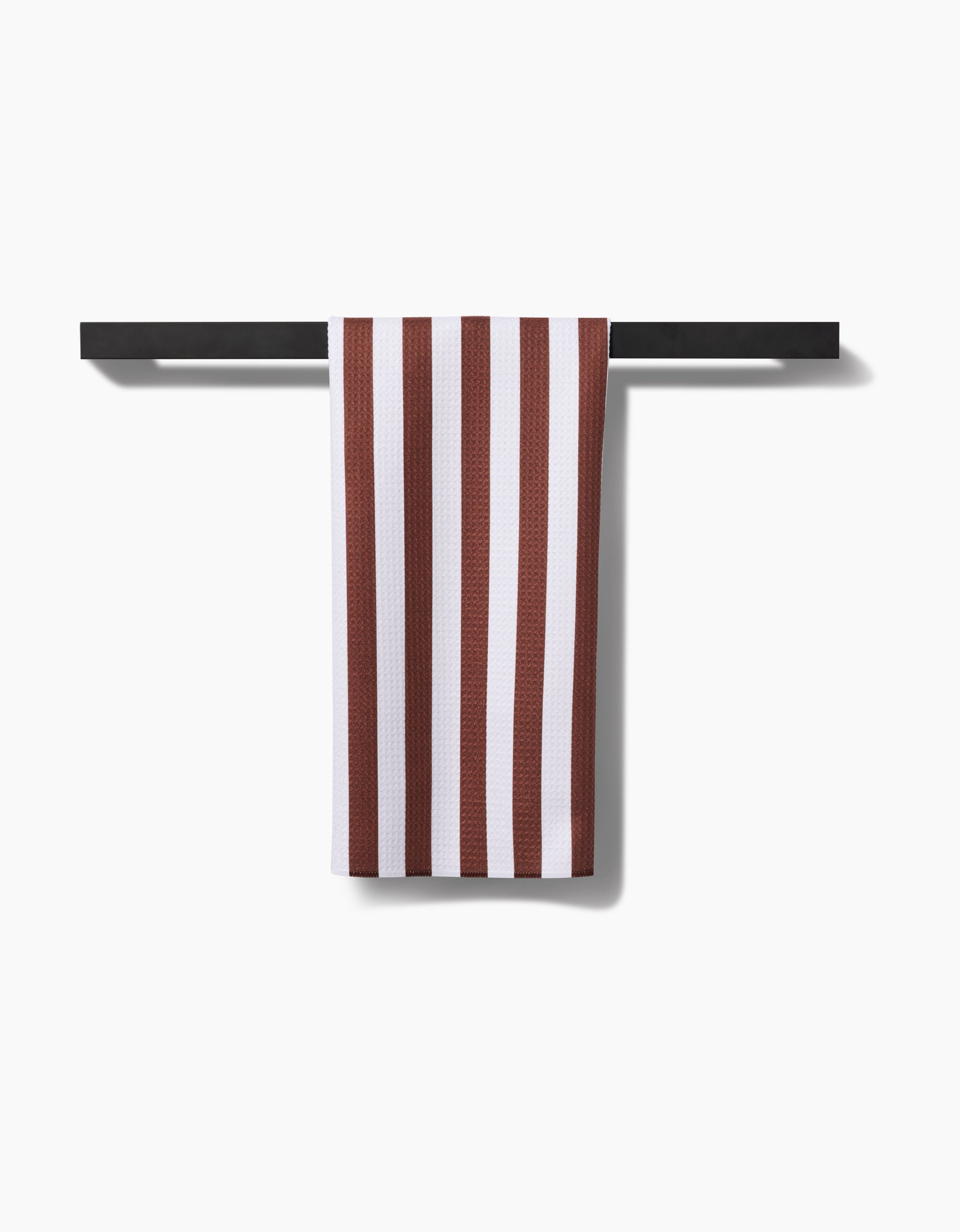 The Toni Stripe tea towel by Kailee Wright, featuring bold red and white vertical stripes and made from recycled materials, hangs neatly on a sleek black towel bar against a plain white background.
