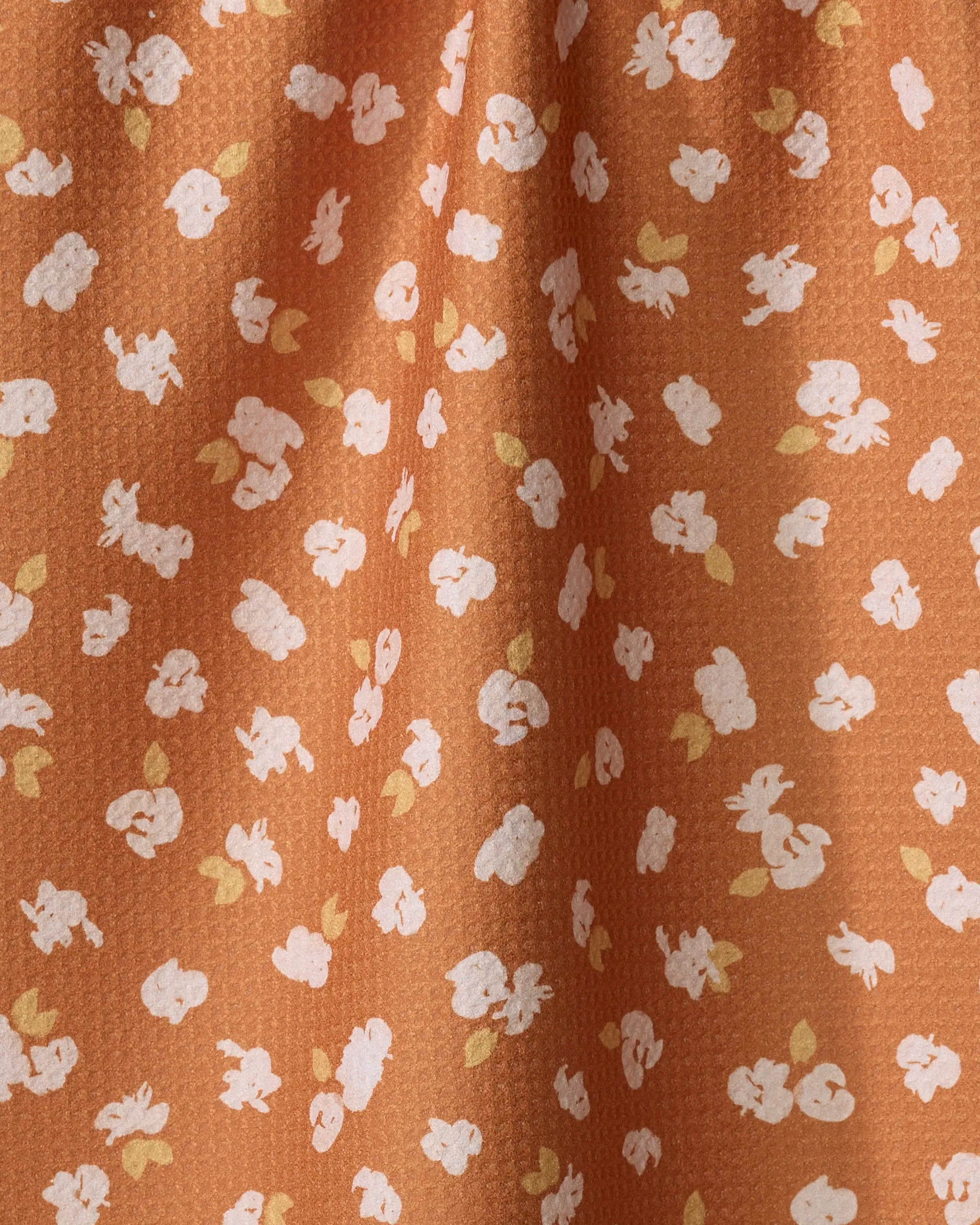 Close-up of Mandy Arroyo’s Tossed Wildflowers Rust fabric: a textured tea towel with small white and yellow flowers on a rust background. Soft folds show its quick-drying quality and enhance the scattered floral design.