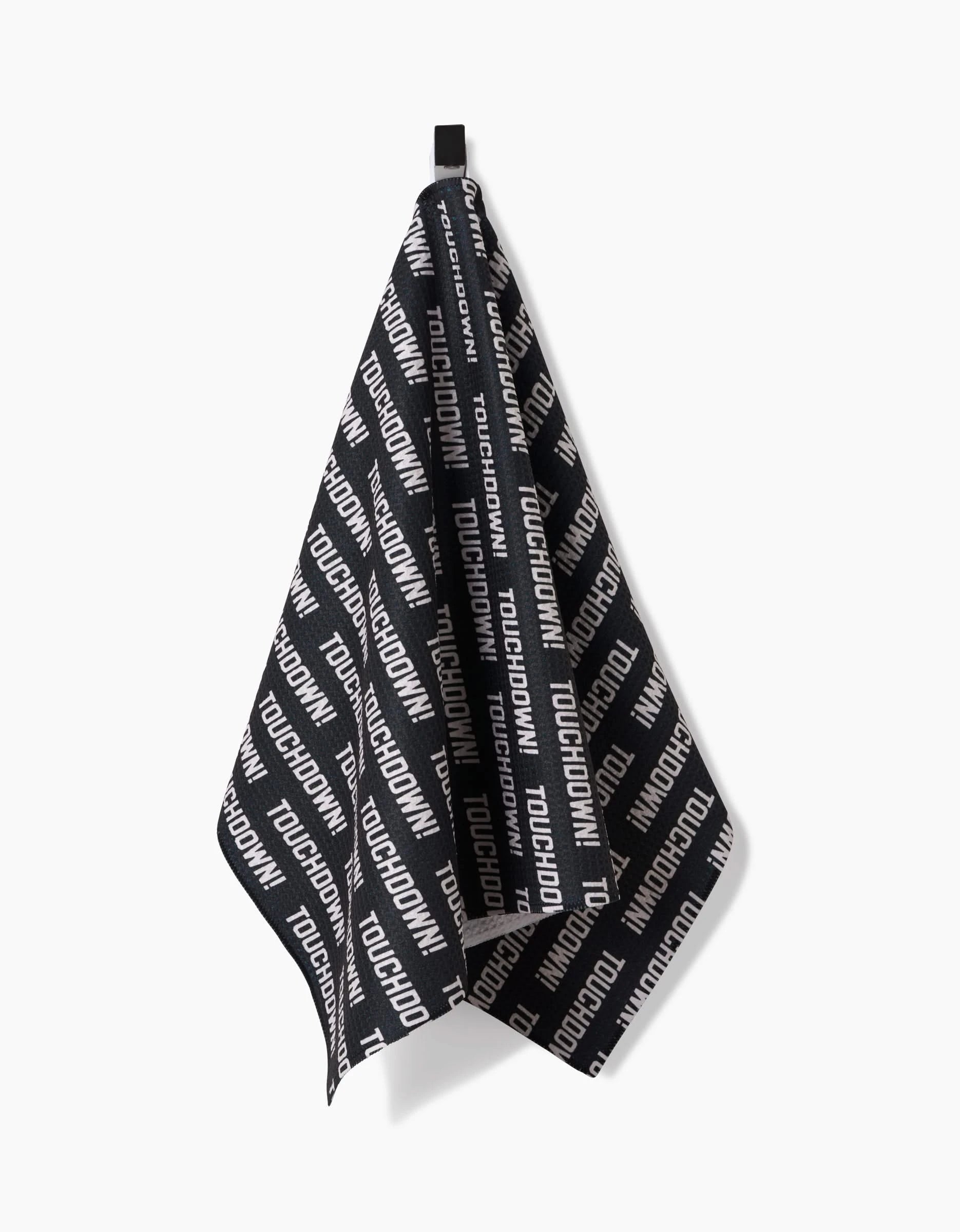 The GEOMETRY Touchdown tea towel, crafted from Geoweave fabric in black with TOUCHDOWN repeated diagonally in white, hangs by a black loop against a plain white background.