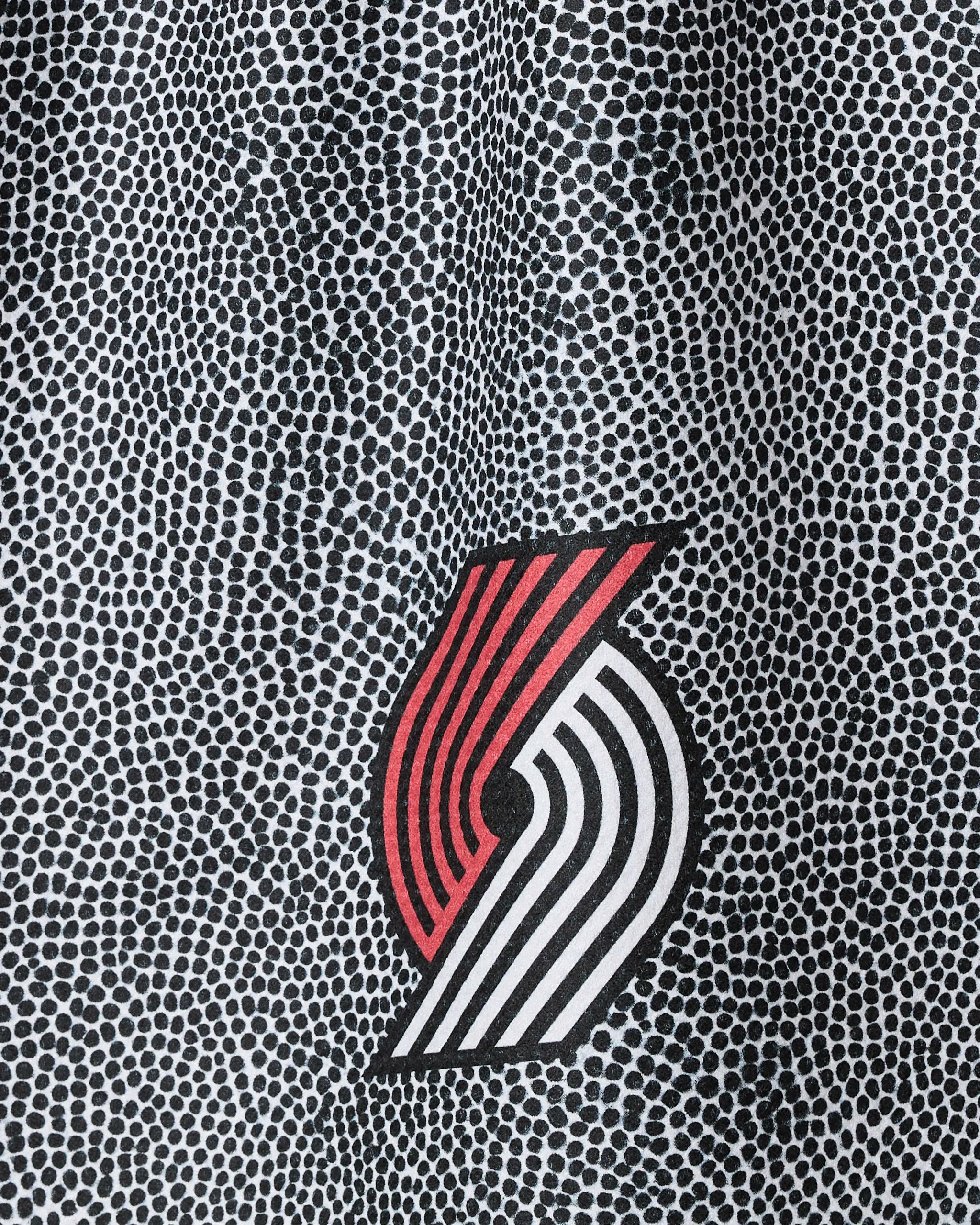 A close-up of the Trail Blazers Grip by NBALAB x Geometry shows a textured black and white spotted background with the Portland Trail Blazers logo of red and white curved lines centered on this sustainable kitchen towel.