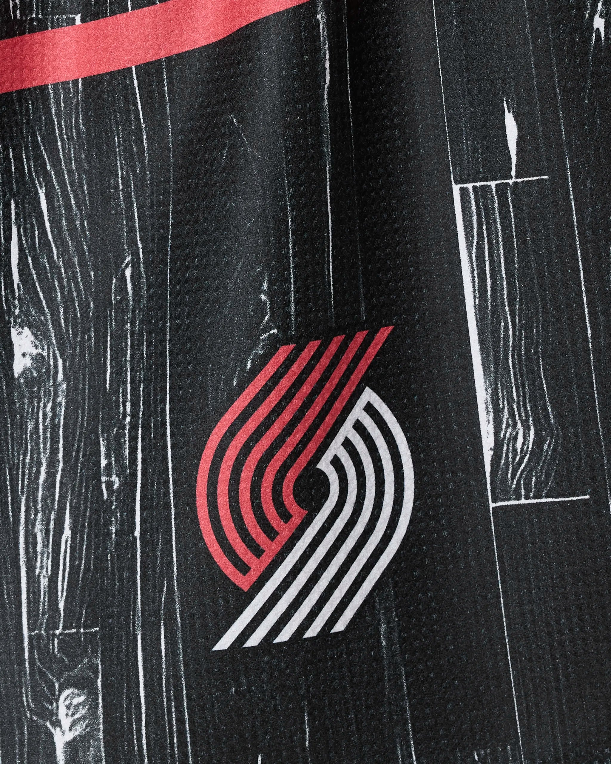 A black woodgrain-patterned fabric featuring a red and white Portland Trail Blazers logo and red stripe—Trail Blazers Zone by NBALAB x Geometry—perfect as official NBA home decor or a sustainable kitchen towel.