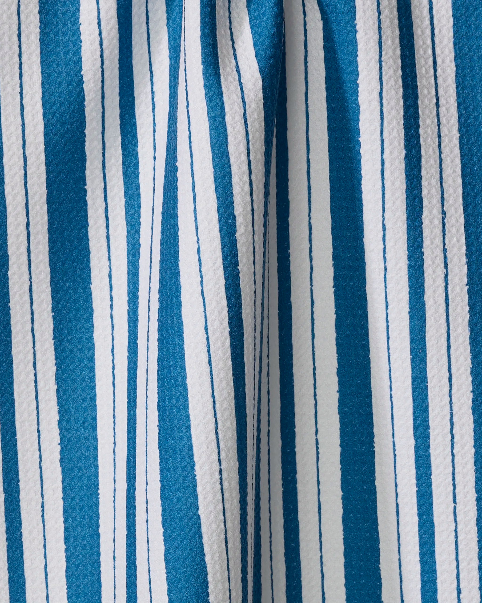 Close-up of blue and white vertical stripes on textured "Trails of Promise" kitchen towel by Ashley Celena. Varying stripe widths create a bold, alternating pattern on the slightly draped fabric.