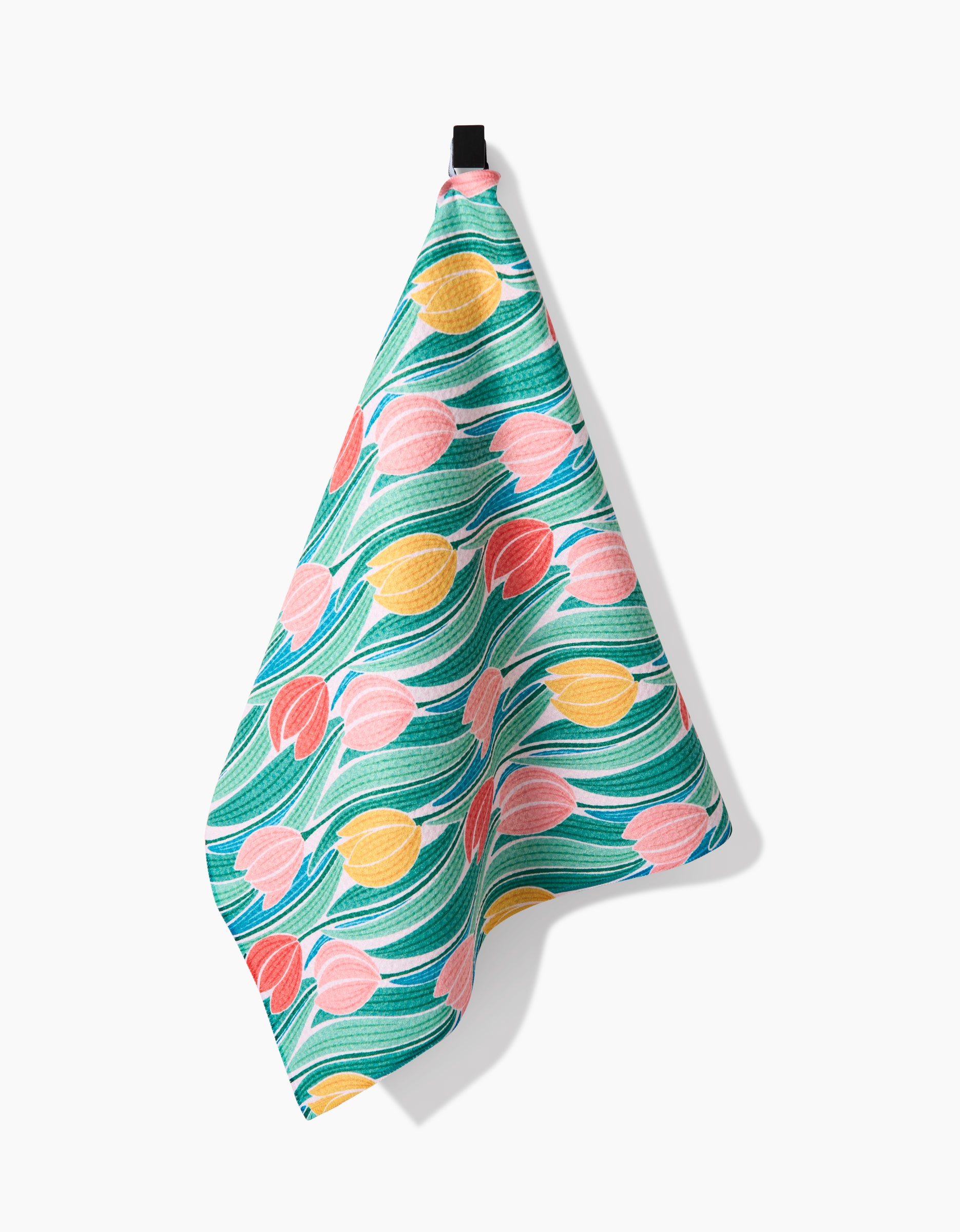 The Tranquil Tulips tea towel by Sarah Daugherty is made from recycled materials and features a colorful pattern of pink, yellow, and red tulips with green leaves. It hangs from a black loop against a white background.