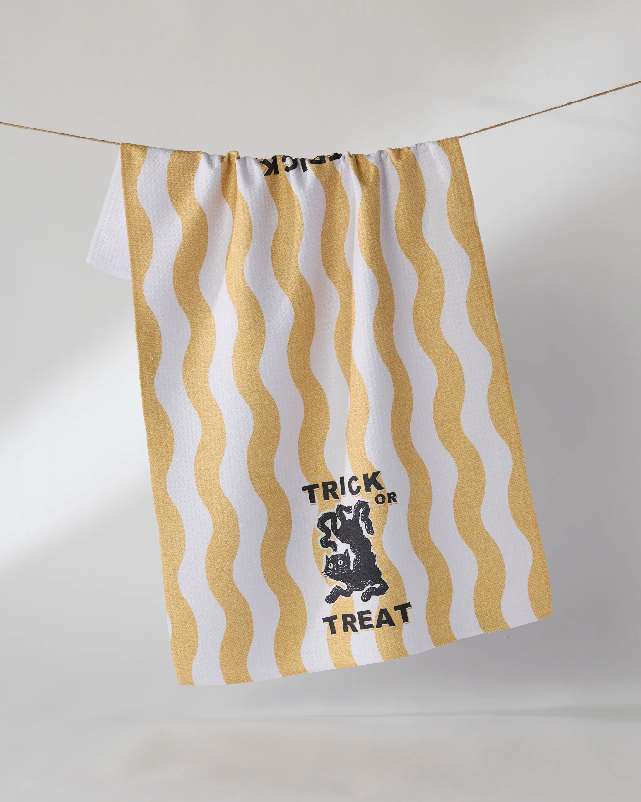 The Geometry Treat Street tea towel, made from recycled materials, features yellow wavy stripes, a black cat graphic, and "TRICK OR TREAT" text on white fabric—perfect for hanging on your clothesline.