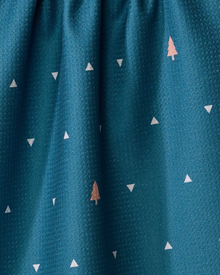The Tree Dots tea towel by Twig + Spark features a teal hue with subtle texture, white triangles, and pink tree shapes. Gathered at the top with gentle folds and crafted from recycled materials for an eco-friendly touch.