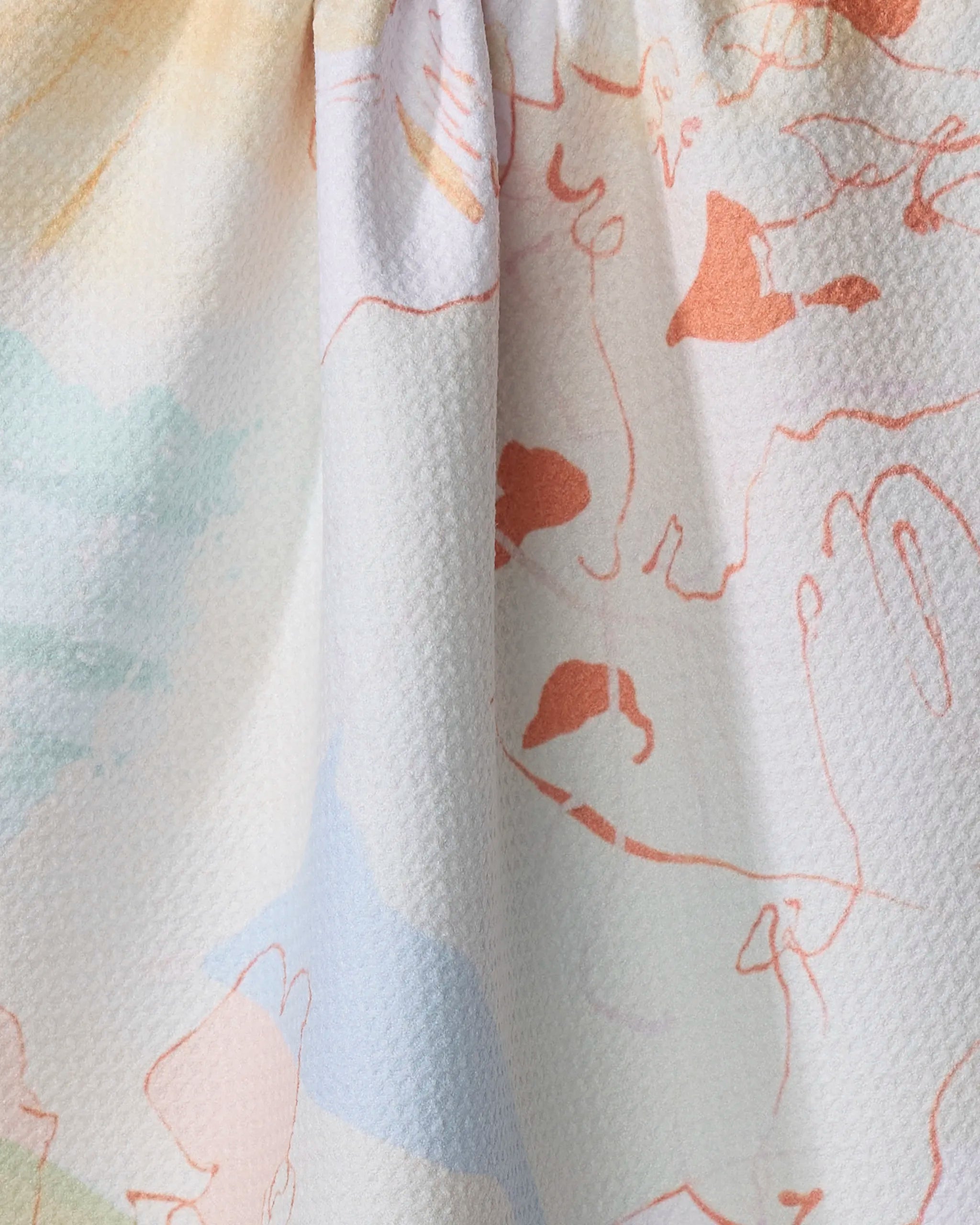 A close-up of Tree House, an ultra-absorbent kitchen towel by Kristina Baker, showing textured white fabric with pastel and orange abstract line drawings—possibly faces and hands—scattered across its surface.