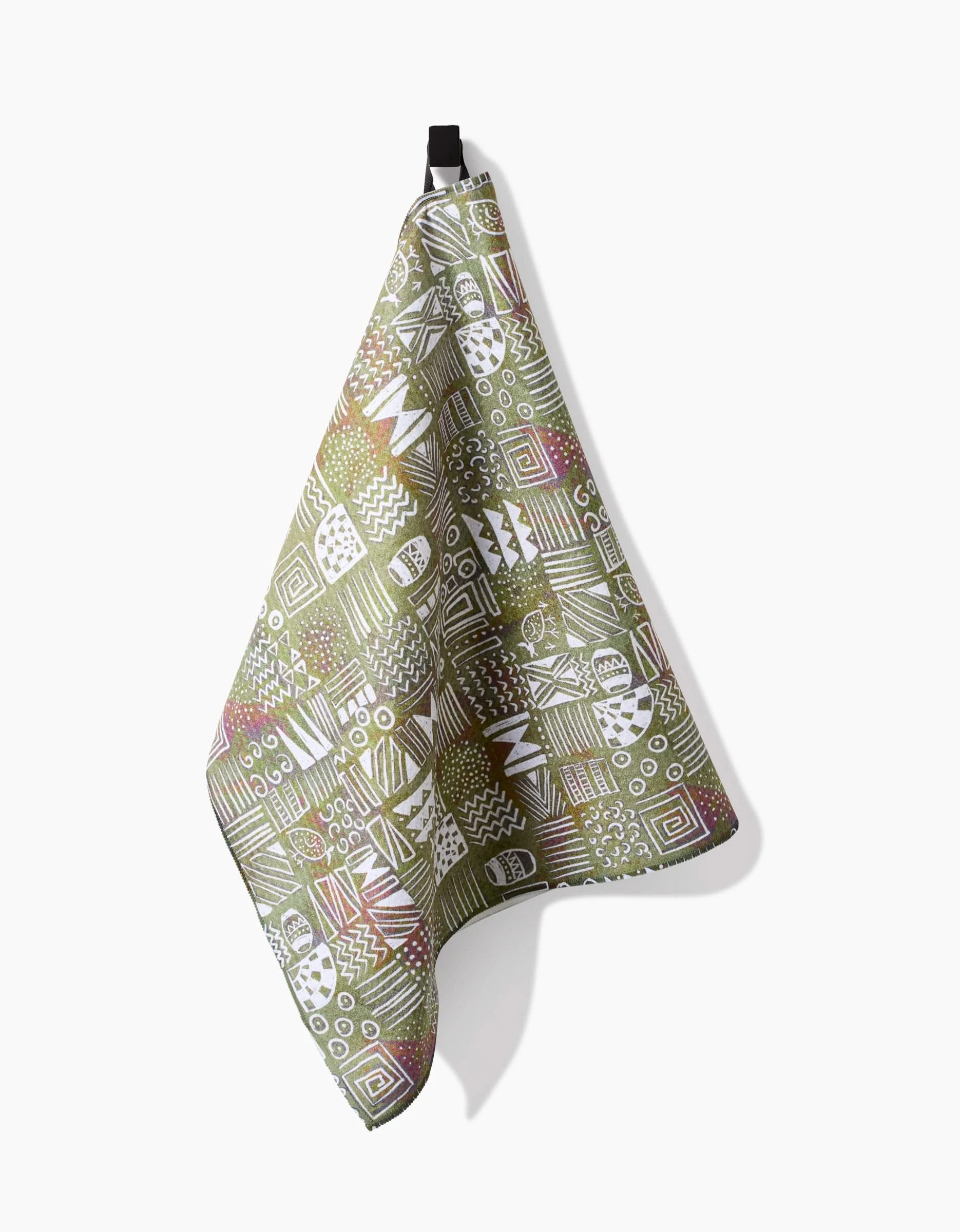 The Tribal Symbols tea towel by Taryn Brennan, made from recycled materials, displays white geometric and abstract patterns on green. It hangs on a black loop against a plain white background, casting a soft shadow.