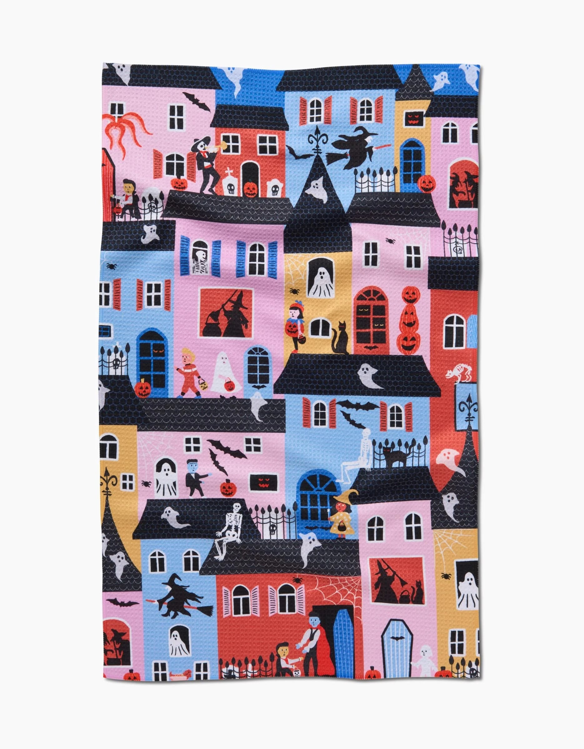 The Trick Or Treat Night kitchen towel by Ceyda Alasar is an eco-friendly, colorful design featuring a lively neighborhood with Halloween houses, playful ghosts, witches, vampires, jack-o’-lanterns, and trick-or-treaters on a vibrant background.