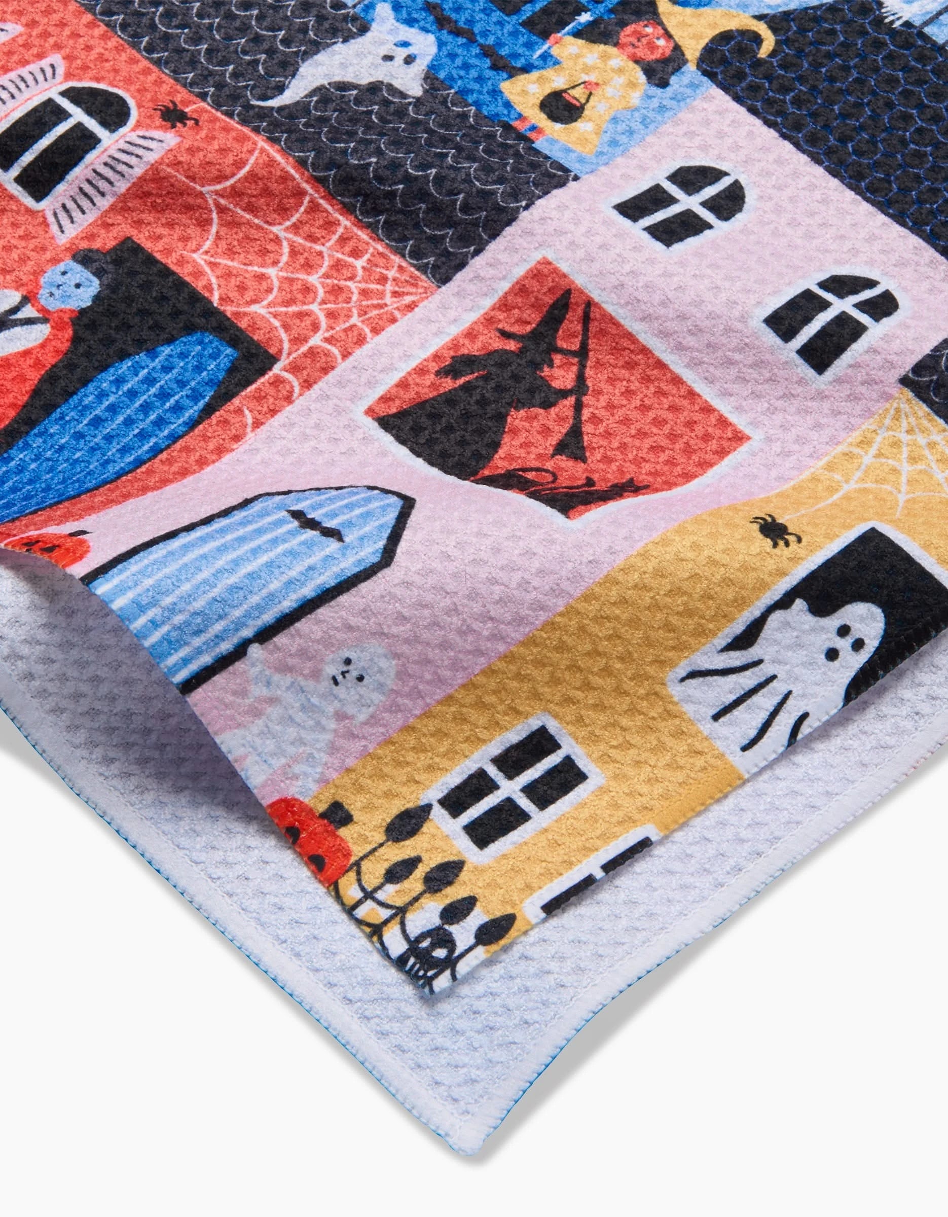 A close-up of Ceyda Alasars Trick Or Treat Night textured, eco-friendly kitchen towel featuring colorful Halloween-themed illustrations—ghosts, witches, cobwebs, and haunted houses—in red, yellow, blue, and black.