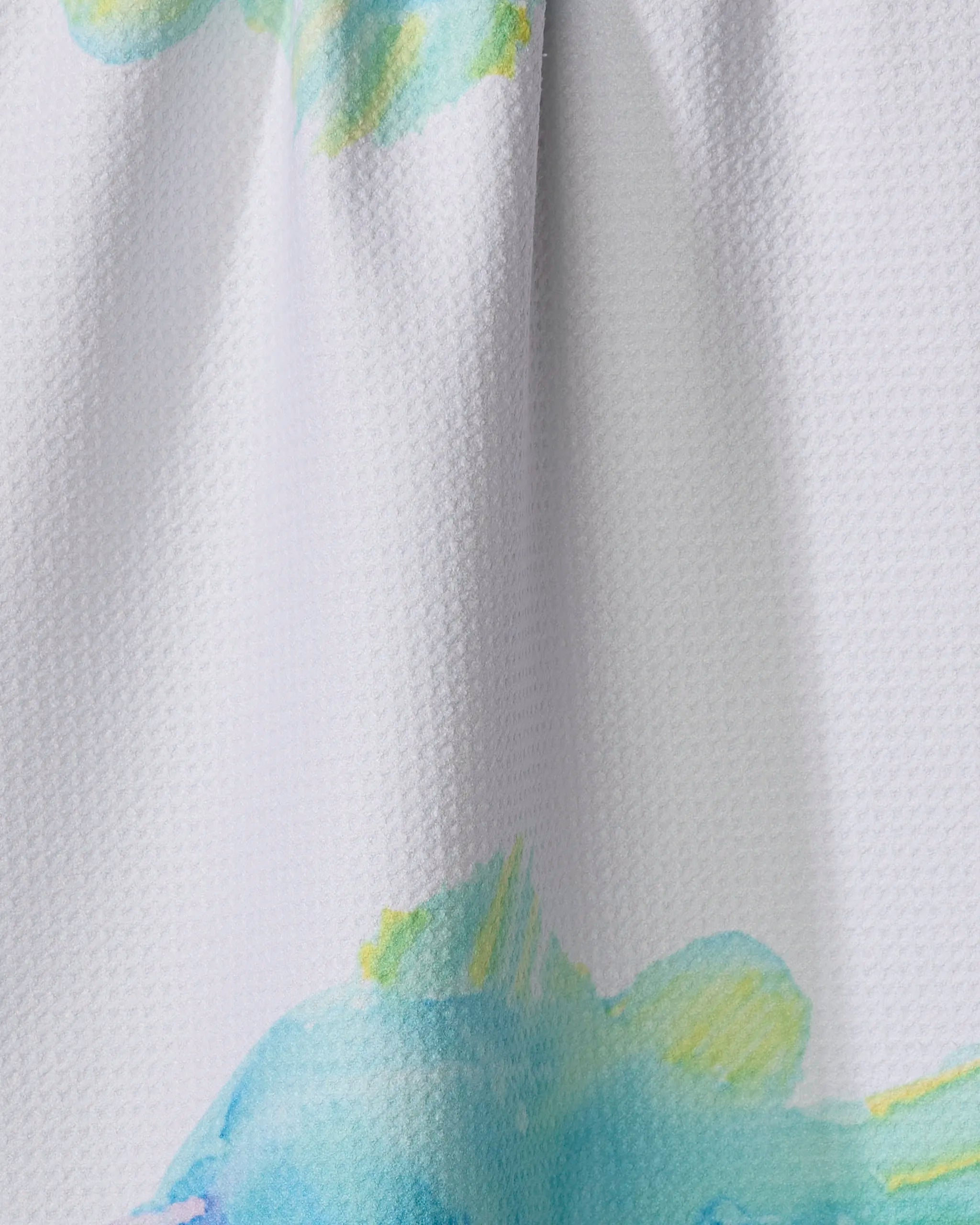 Close-up of Trey Jolley's "Tropical Twins"—a textured, white recycled kitchen towel with a soft watercolor print in pastel blue, green, and yellow, featuring abstract fish-like shapes.