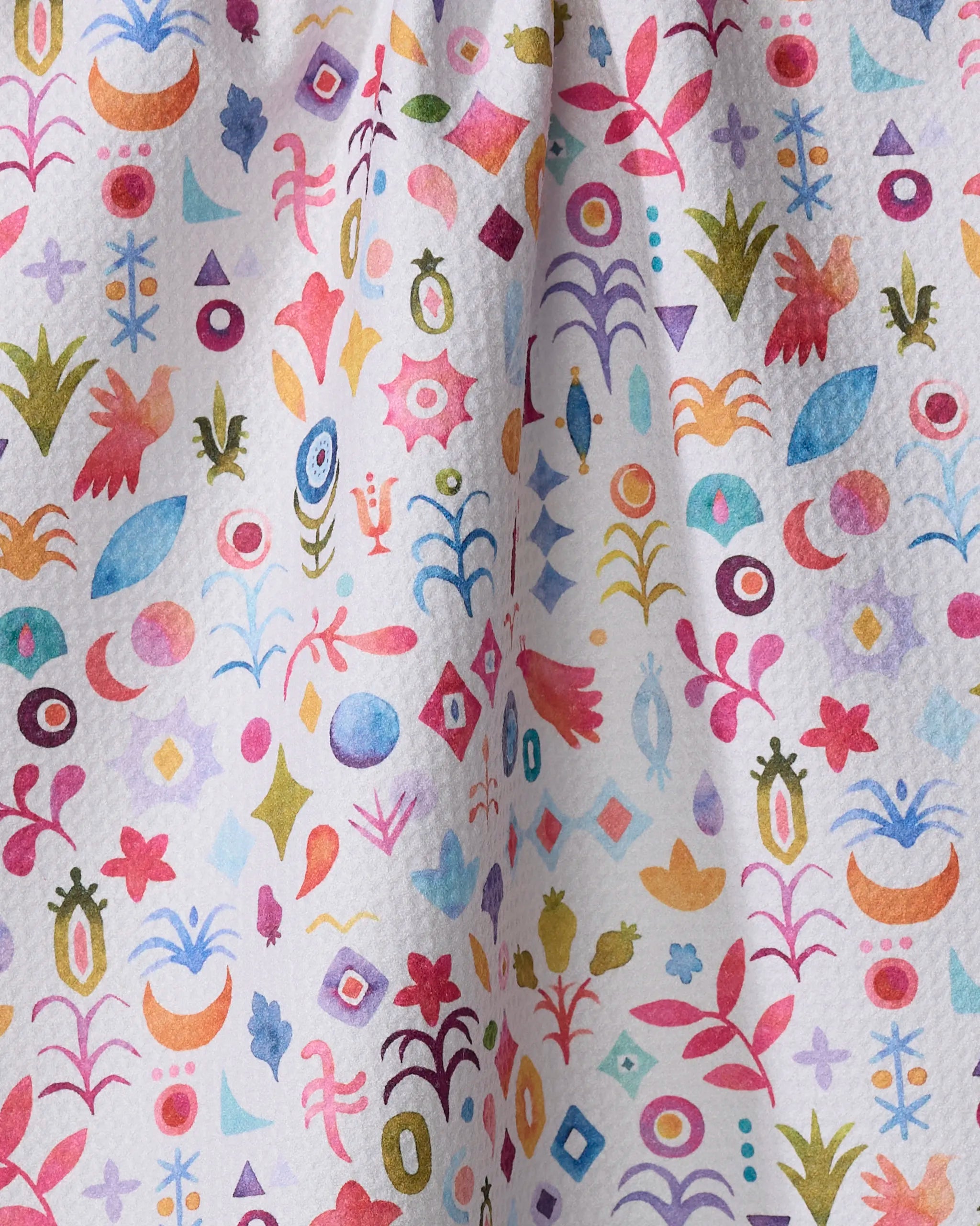 Tula by Maayan Alper-Swan features a whimsical pattern of abstract shapes, flowers, leaves, birds, and geometric forms in pink, blue, green, and yellow on a textured white ultra-absorbent tea towel made from recycled materials.