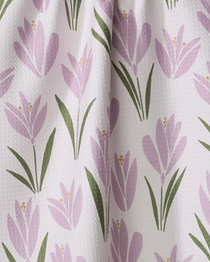 A close-up of a fabric tea towel by Janna Sue Design, with a textured surface and a repeating pattern of tulip bulbs and green leaves on a light background.