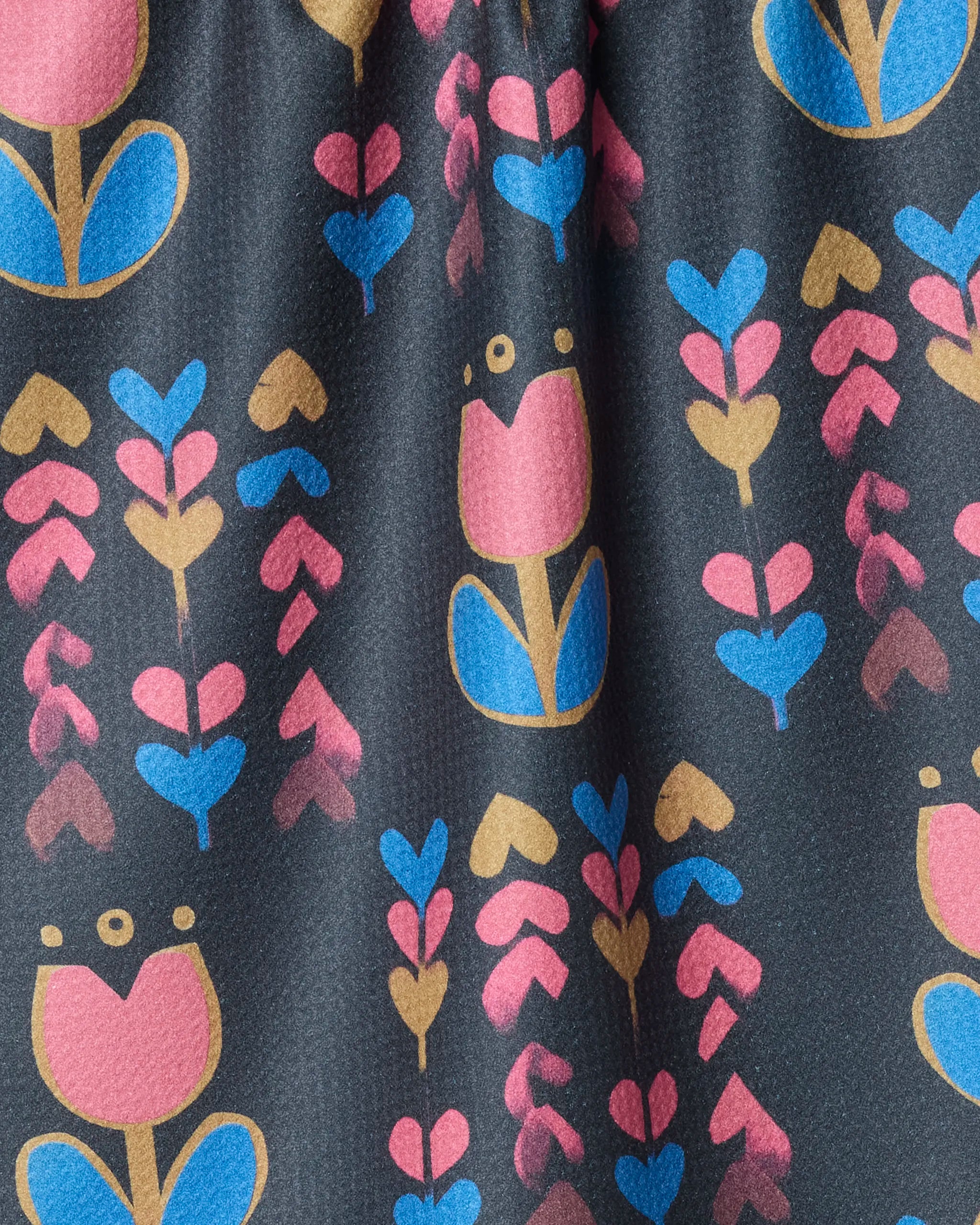 The Geometry Tulip Patch tea towel features a playful, geometric floral pattern with pink, blue, and yellow flowers and leaves in vertical rows on dark fabric, crafted from recycled materials.