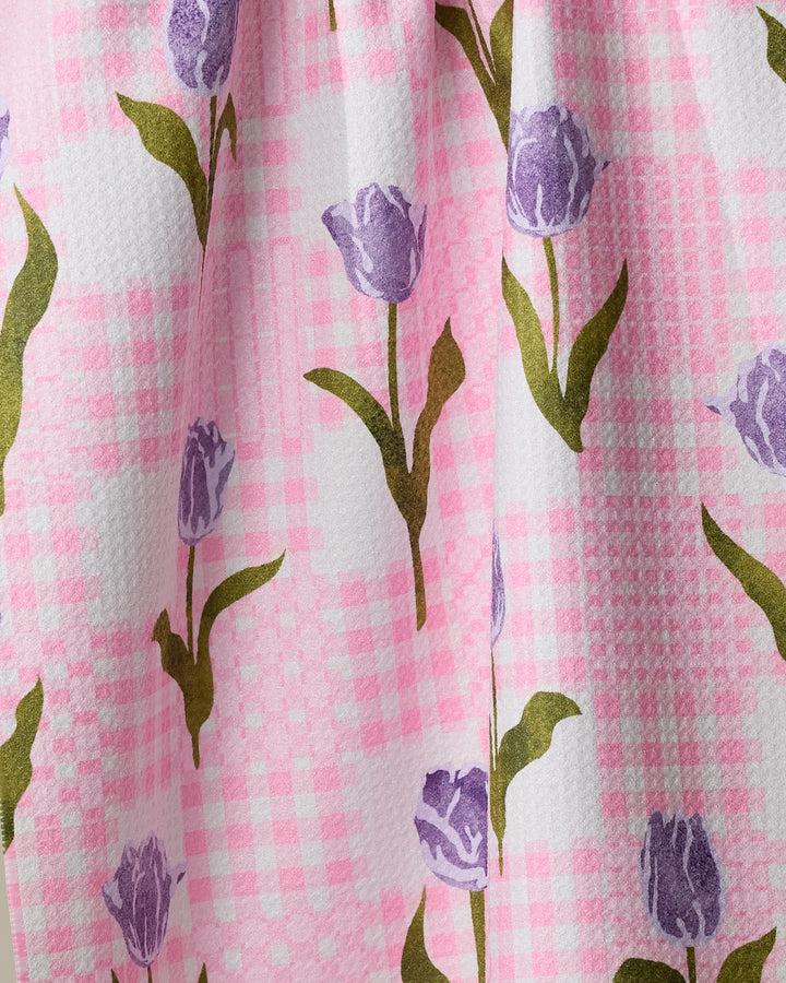 Close-up of Geometry's Tulip Town tea towel, made from recycled materials, featuring a pink and white checkered pattern with purple tulips and green stems.