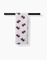 The Turkey Trot tea towel by Vaishali Design Studio hangs on a black rod, showcasing a quick-drying fabric with a repeating pattern of turkeys with red heads and brown feathers.