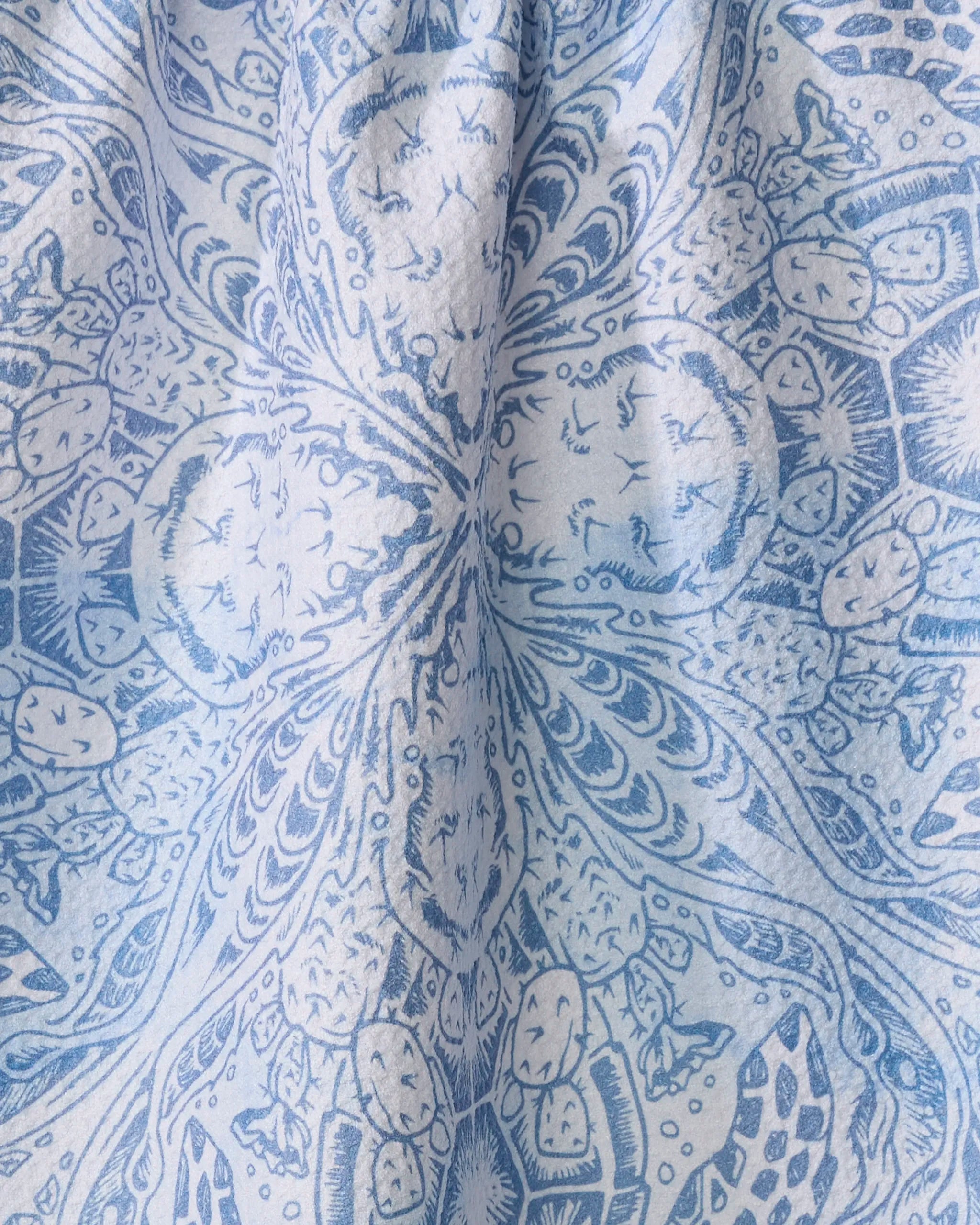 Close-up of the Skye Walker "Turtle" tea towel in blue and white, showcasing an intricate, symmetrical pattern with abstract, floral, and geometric motifs. The fabric is slightly gathered at the center.