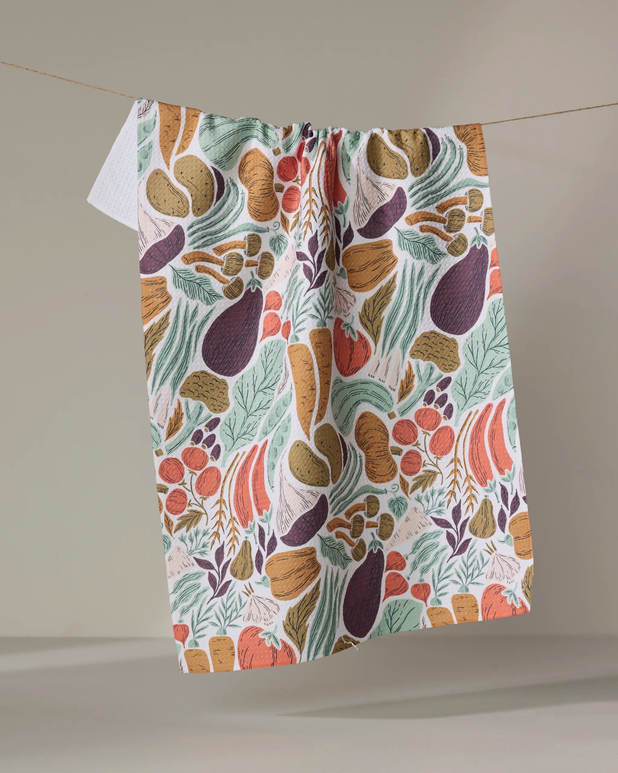 The Twila tea towel by Amy MacCready features an abstract vegetable pattern in orange, green, purple, and brown. Made from recycled materials, it adds an eco-friendly touch to your kitchen decor.