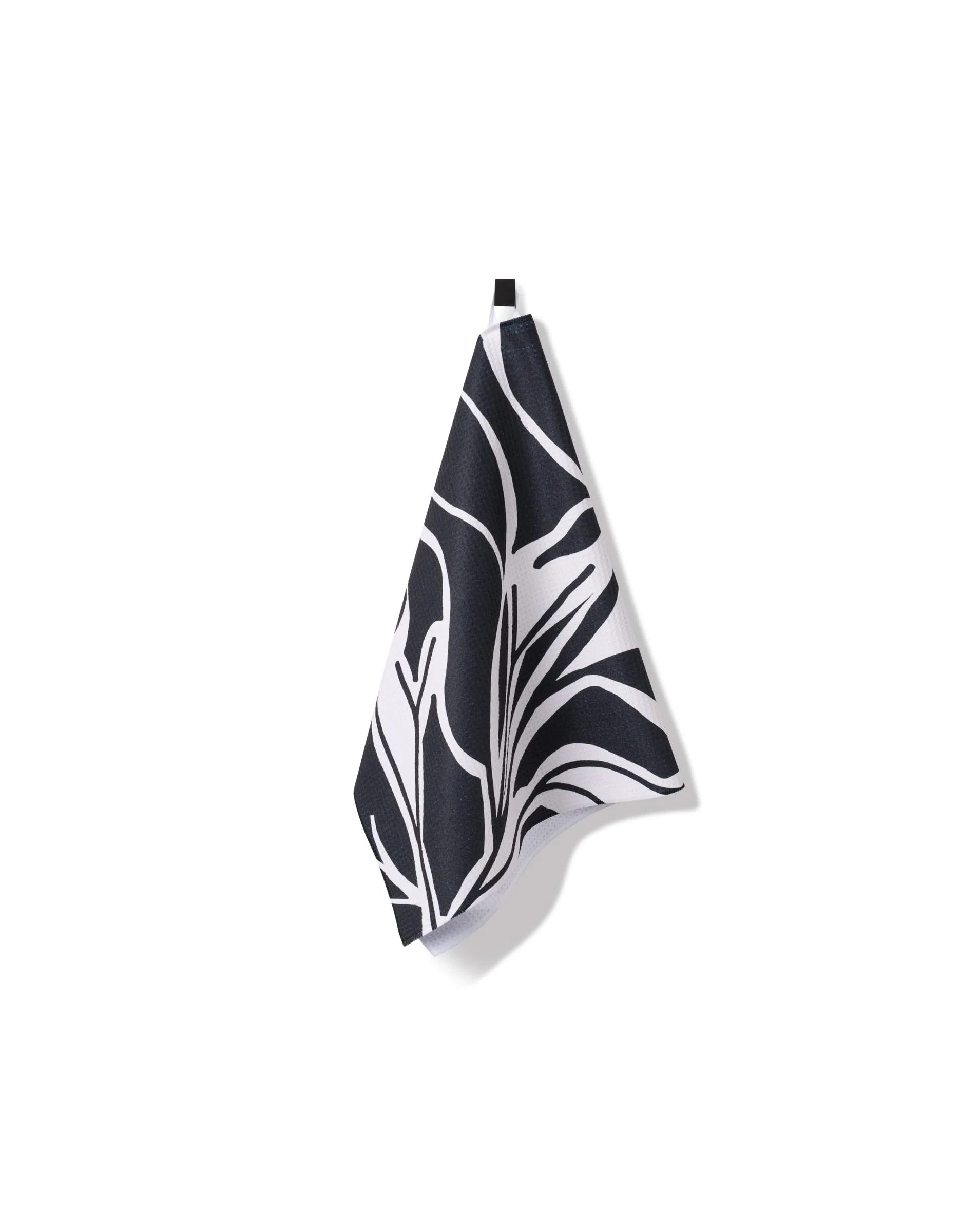 The Ash Cascade Twilight Plant kitchen towel, featuring an eco-friendly black and white abstract leaf design, hangs from a small loop against a plain white background.