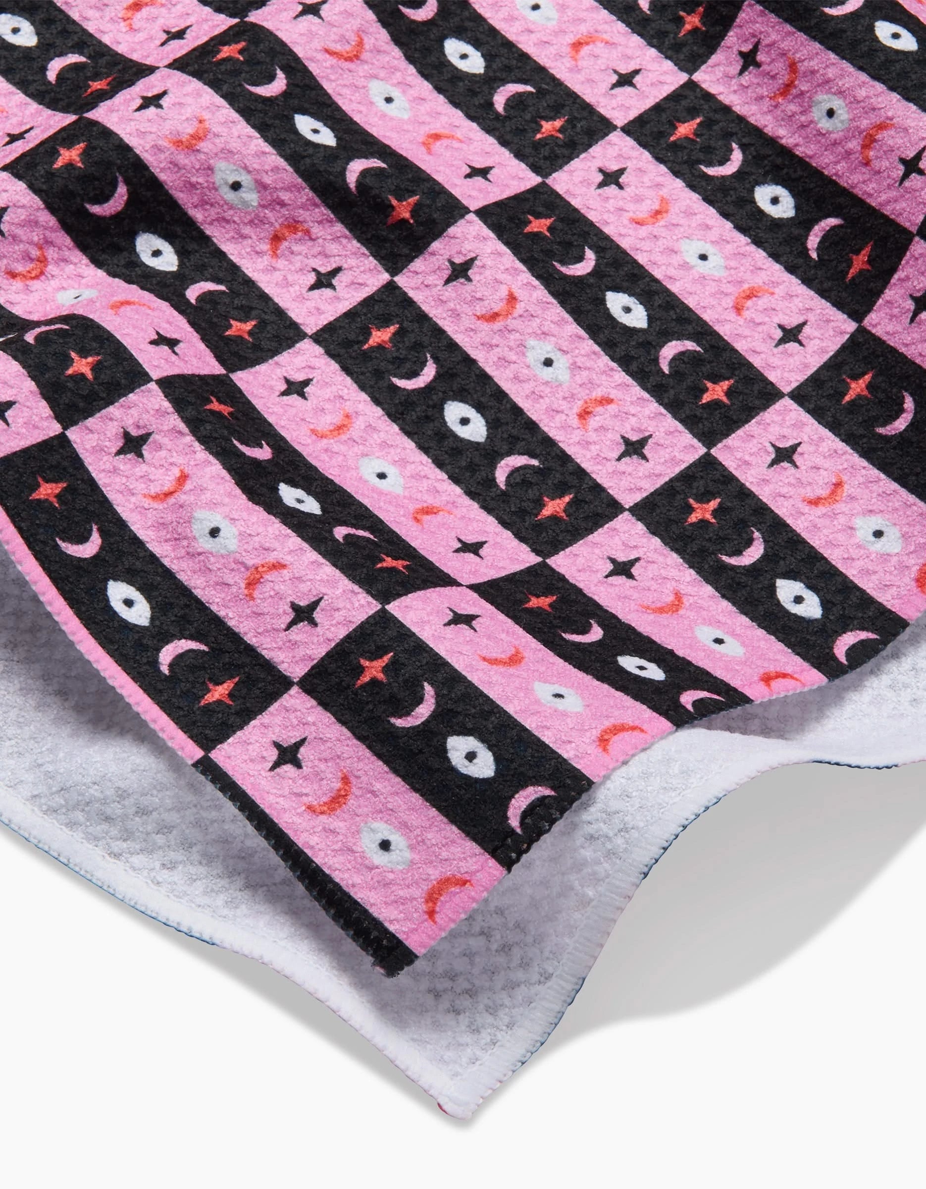 A close-up of the Twinkling Eye Tea Towel by Laura Supnik, showing pink and black stars, crescent moons, and eye patterns on soft Geoweave fabric.