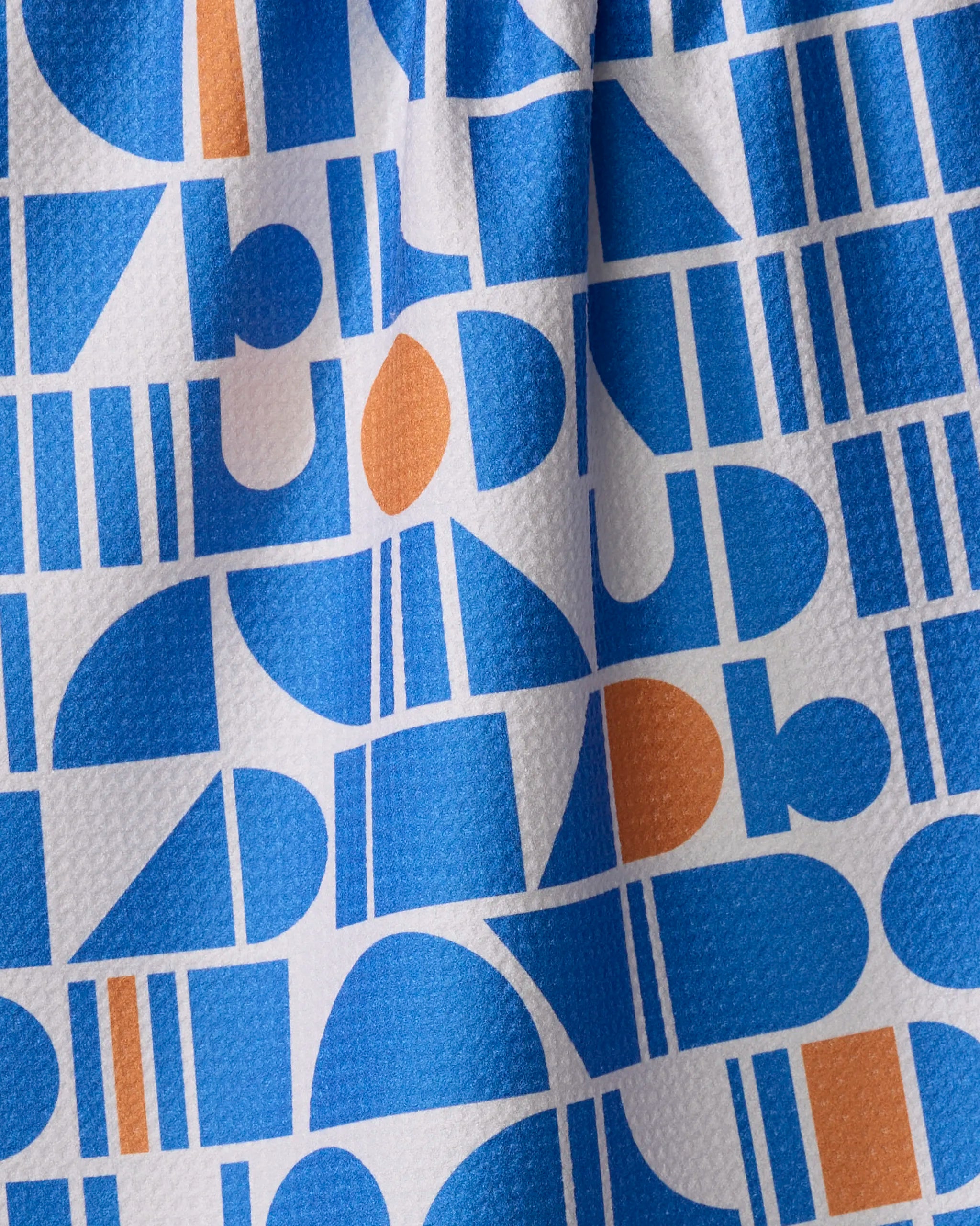 The Ultra Marine Harmony tea towel by Happy Hemera features a colorful geometric pattern of blue and orange shapes on white. Ultra-absorbent and slightly wrinkled, it adds a charming touch to any kitchen.