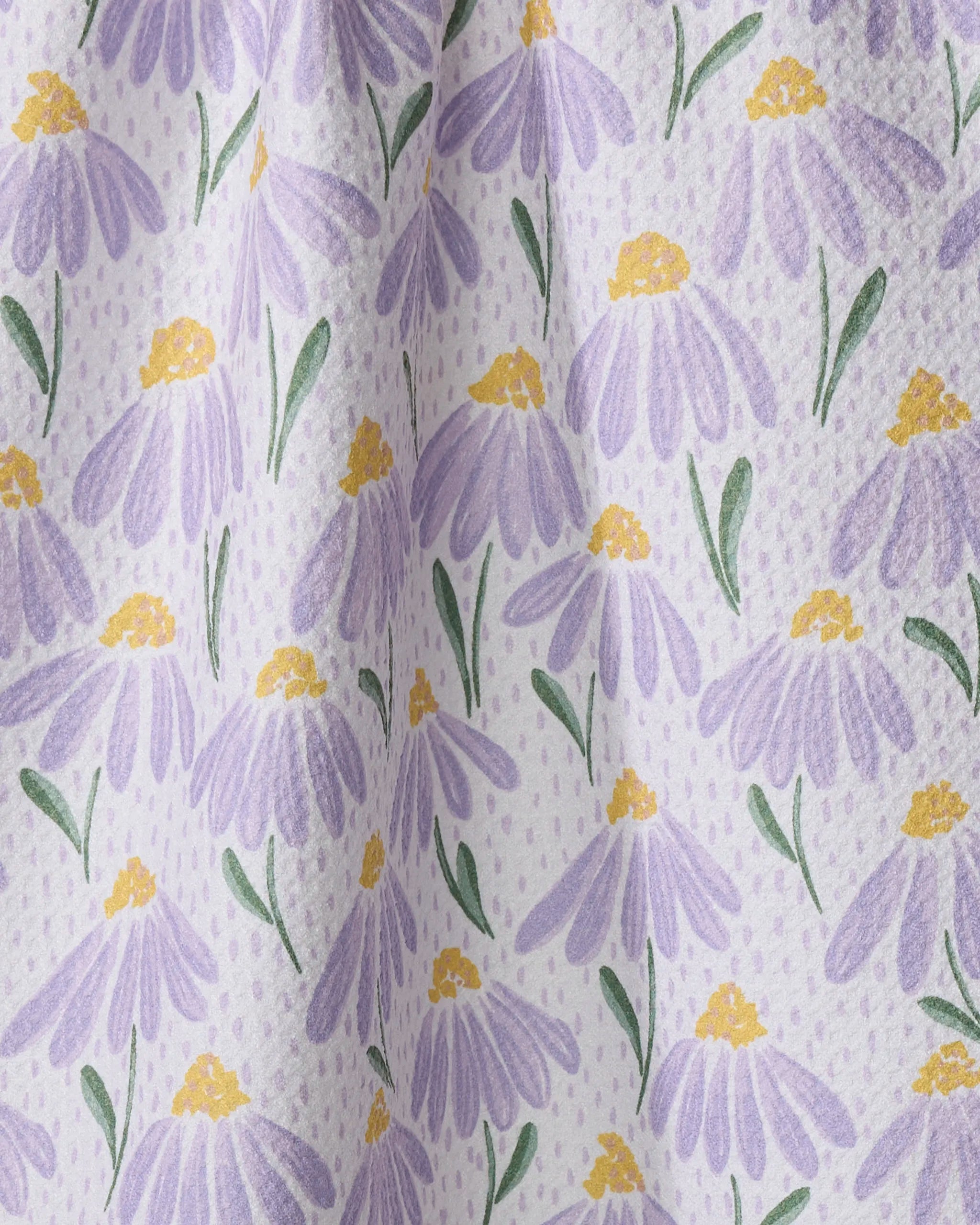 A close-up of Hufton Studio's Upside Down Daisy tea towel, made from recycled materials, shows soft fabric folds and a white background decorated with a repeating pattern of purple daisies with yellow centers and green leaves.