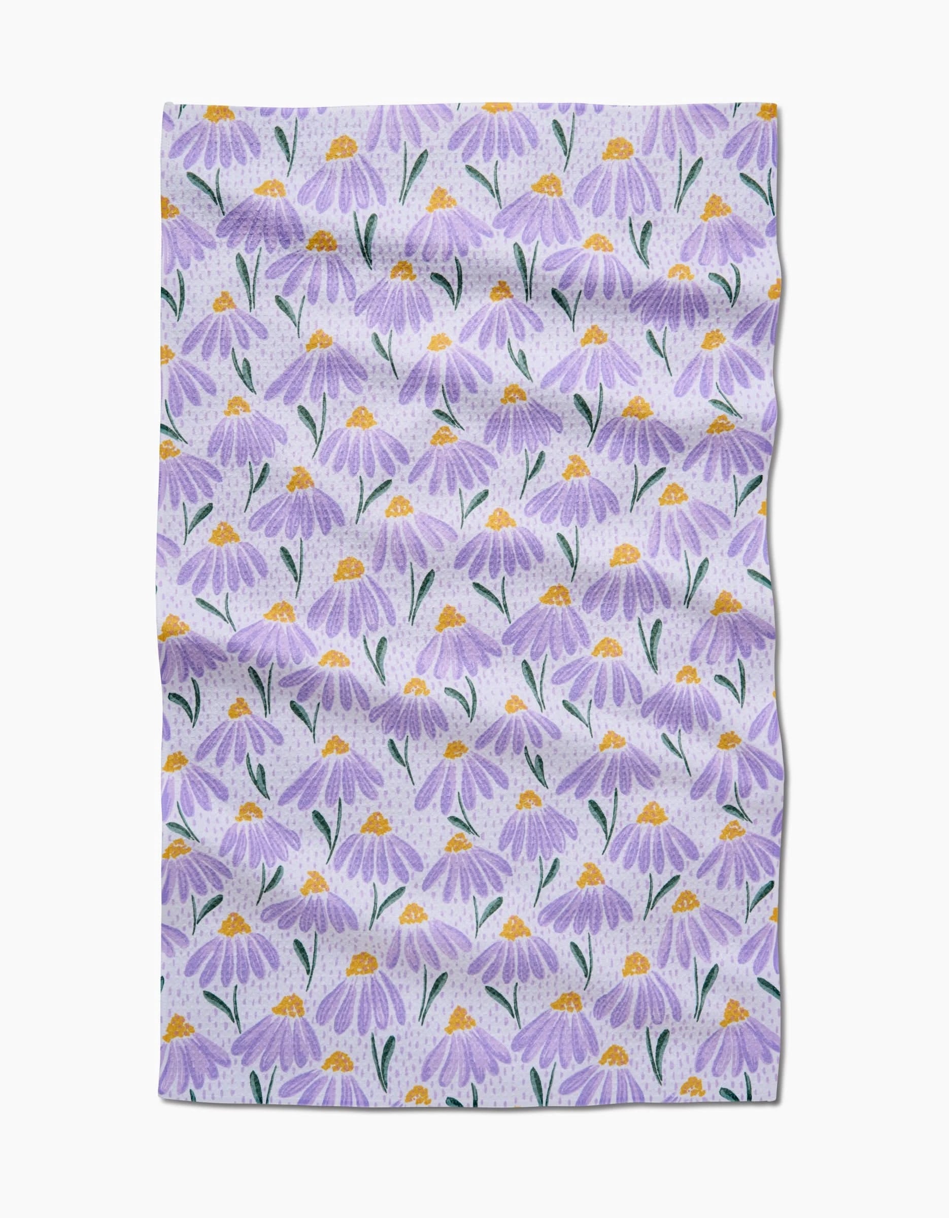 The Upside Down Daisy tea towel by Hufton Studio is made from Geoweave fabric and features a repeating pattern of purple daisy-like flowers with yellow centers and green leaves on a light background.